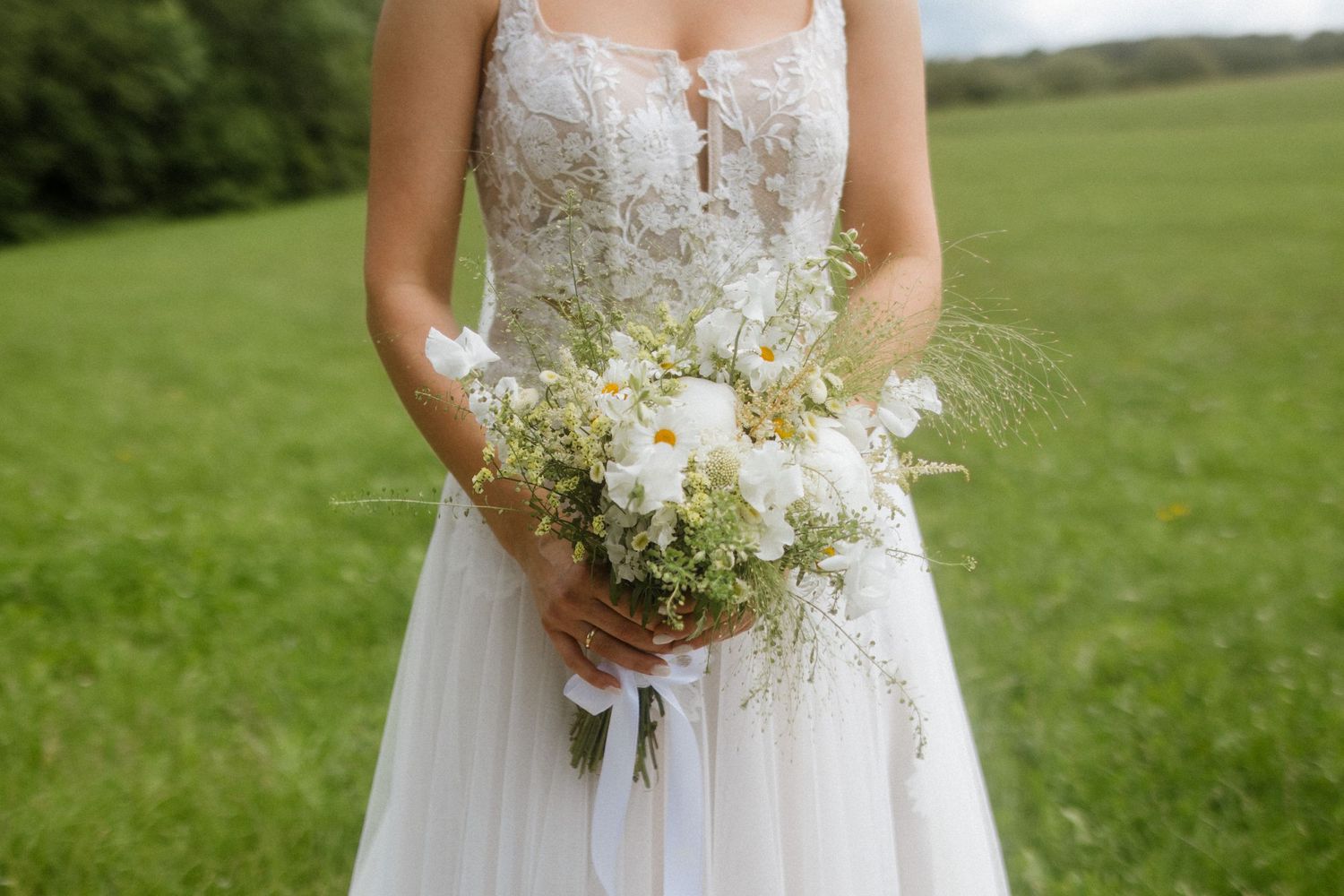 Close-up of bride's torso in lace wedding dress holding white and green floral bouquet.