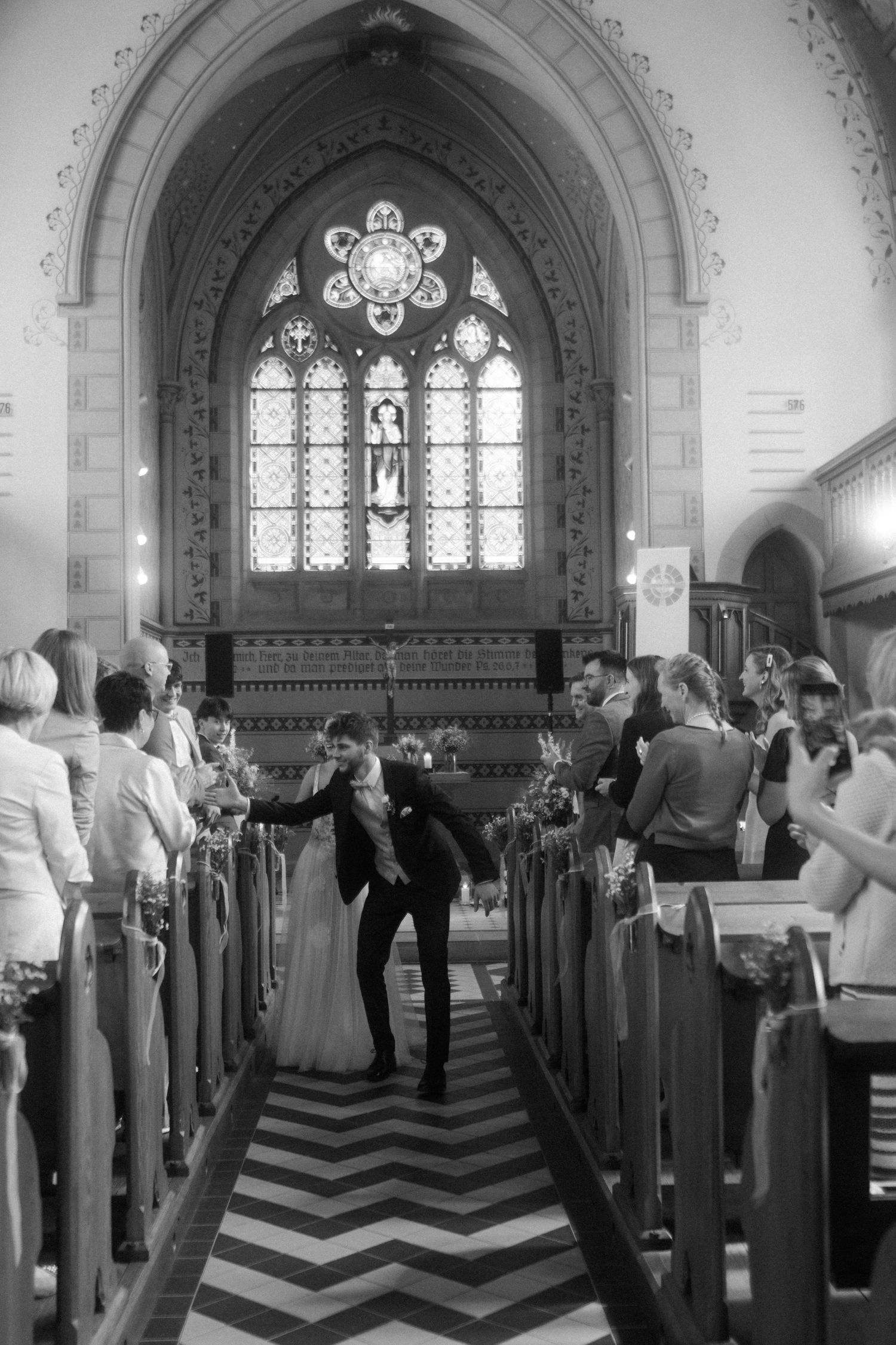 Black and white photo of newlyweds kissing in church aisle during ceremony.