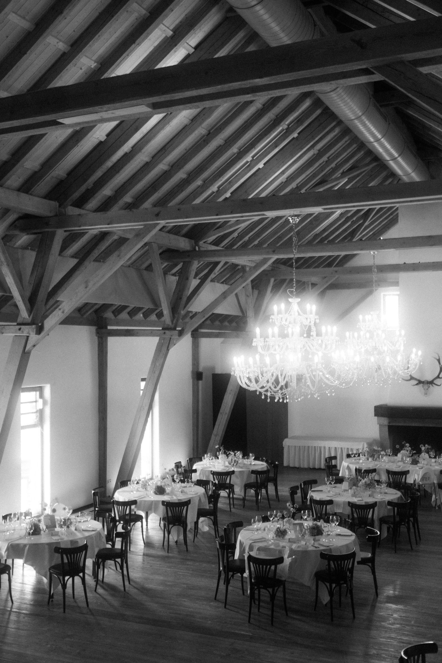 Elegant reception hall with exposed wooden beams and crystal chandeliers in black and white.