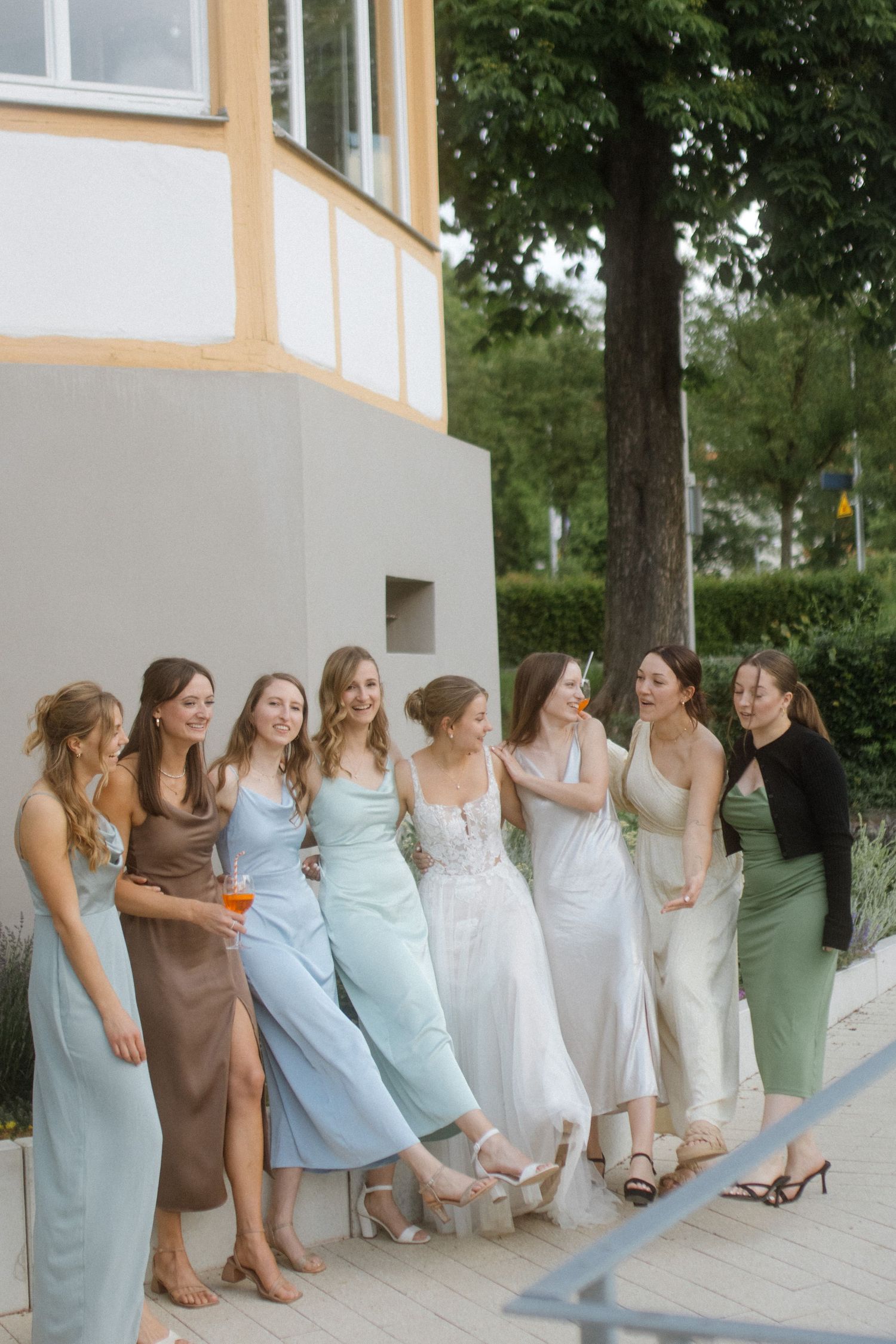 Bridal party in coordinated dresses poses together outside building.