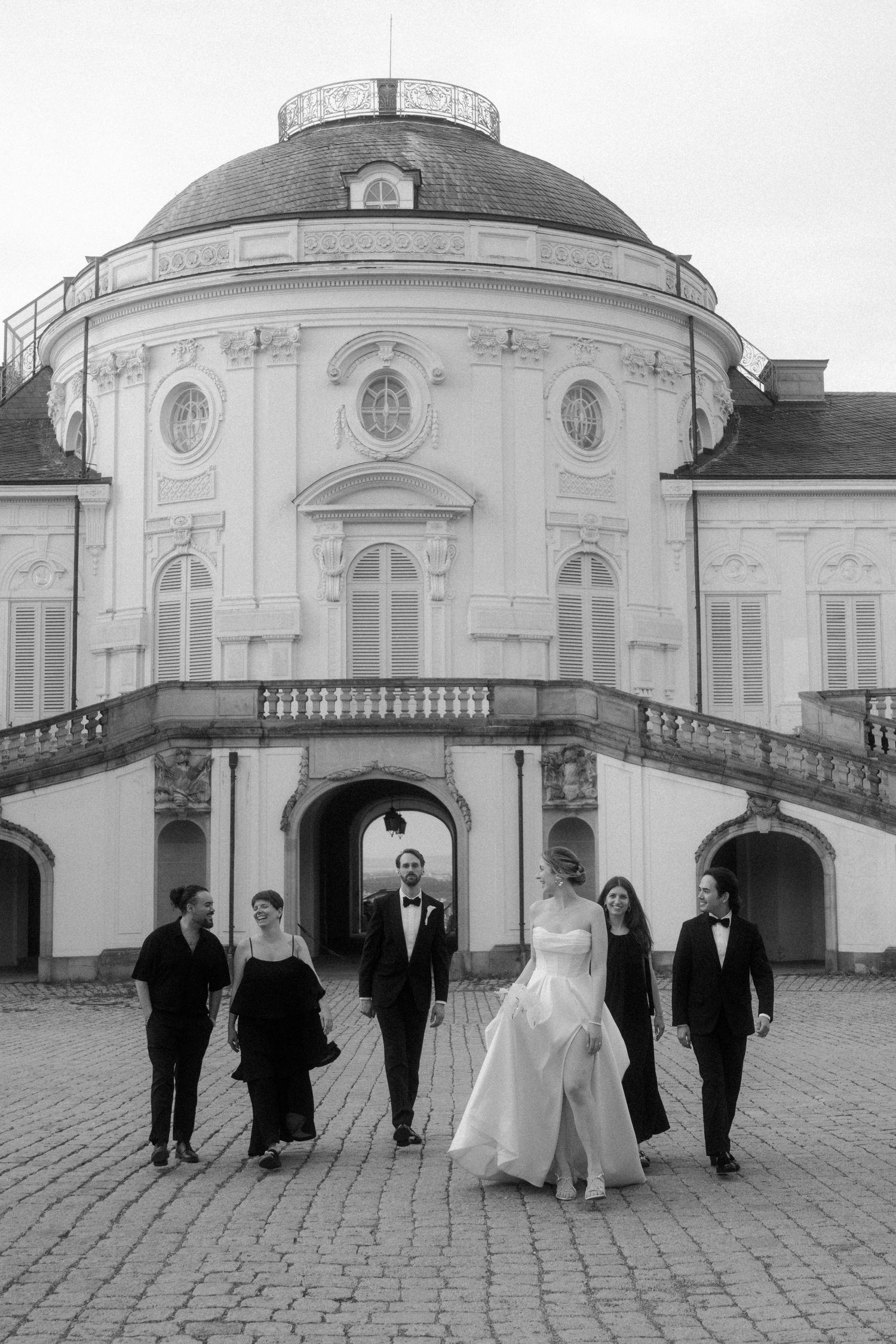 Wedding party walking in formation across cobblestone courtyard of historic building.