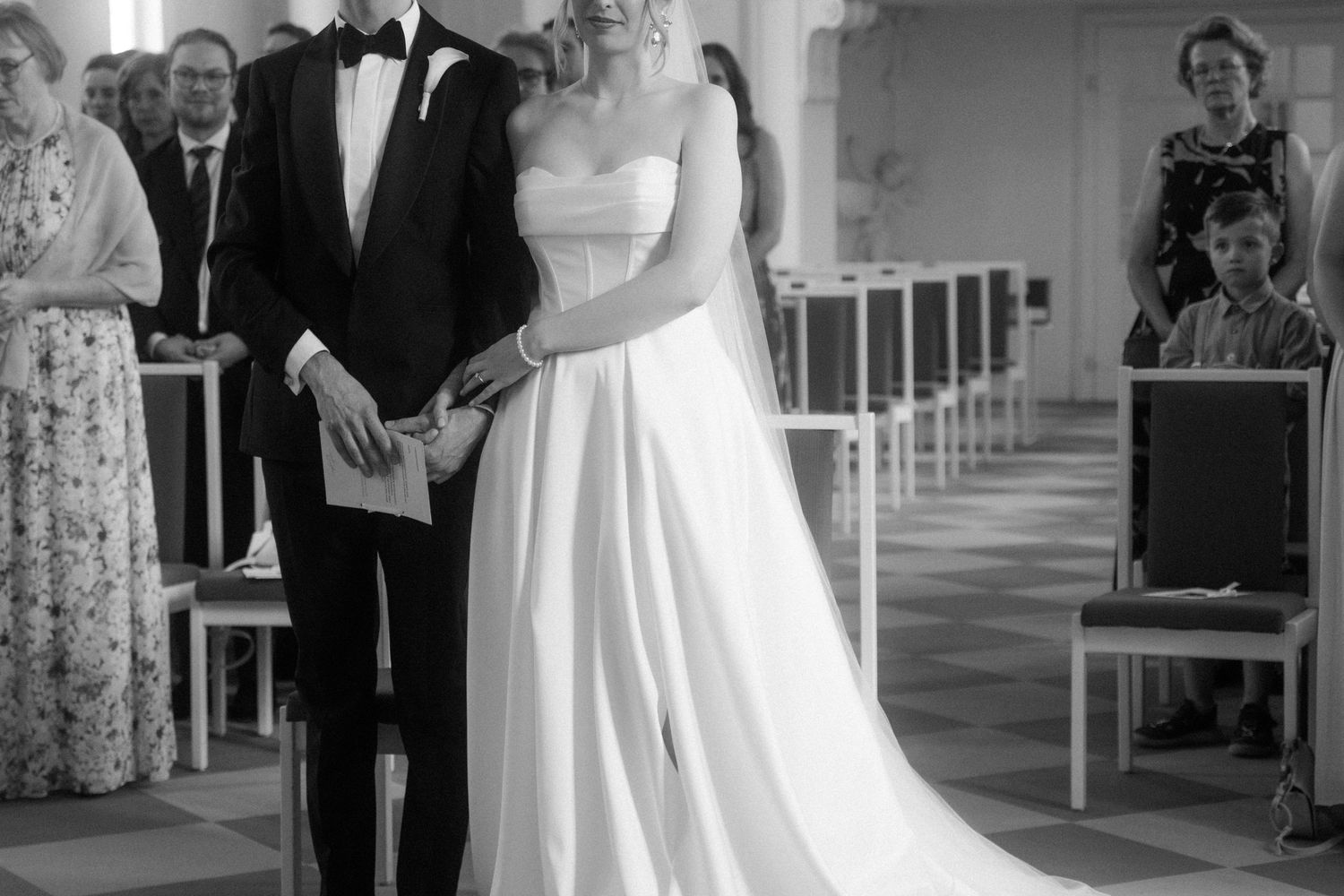Classic black and white wedding ceremony photo in an elegant white hall.