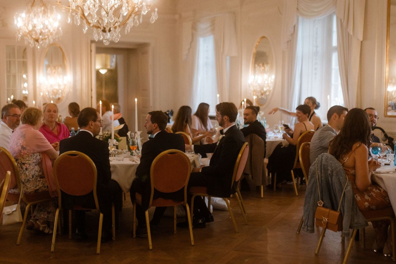 Elegant wedding reception hall with crystal chandeliers and guests seated at round tables.