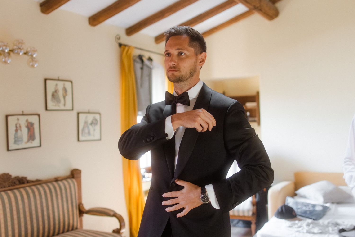 A person in formal attire gestures dramatically in a room with exposed ceiling beams.