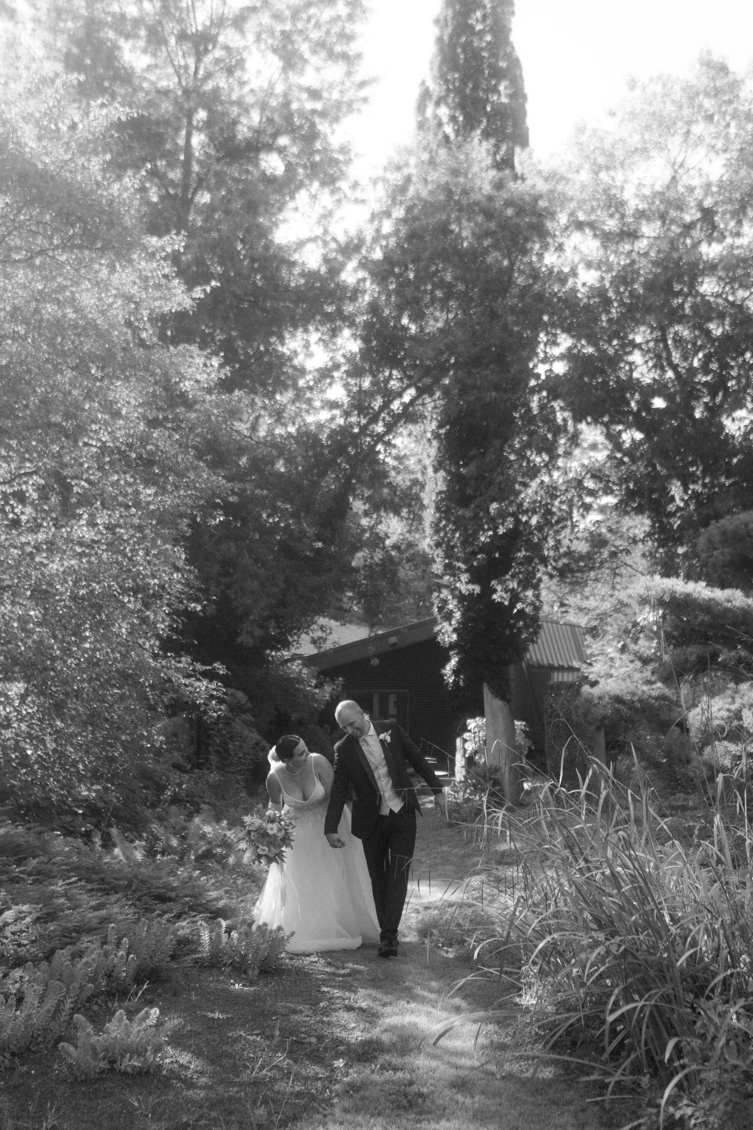 Black and white capture of a wedding couple strolling through a scenic garden pathway.