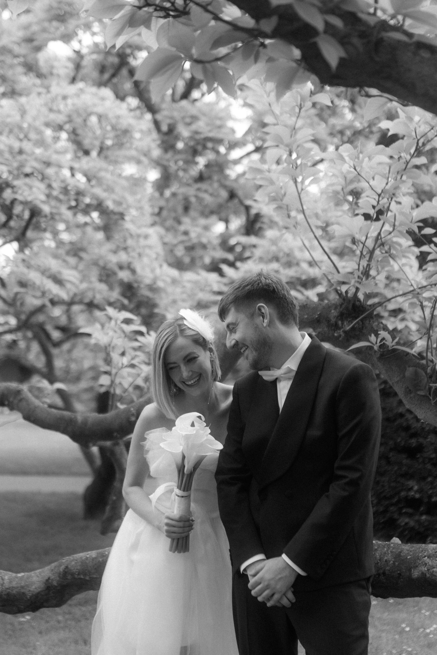 Black and white candid photo of a couple laughing together in a lush garden setting.