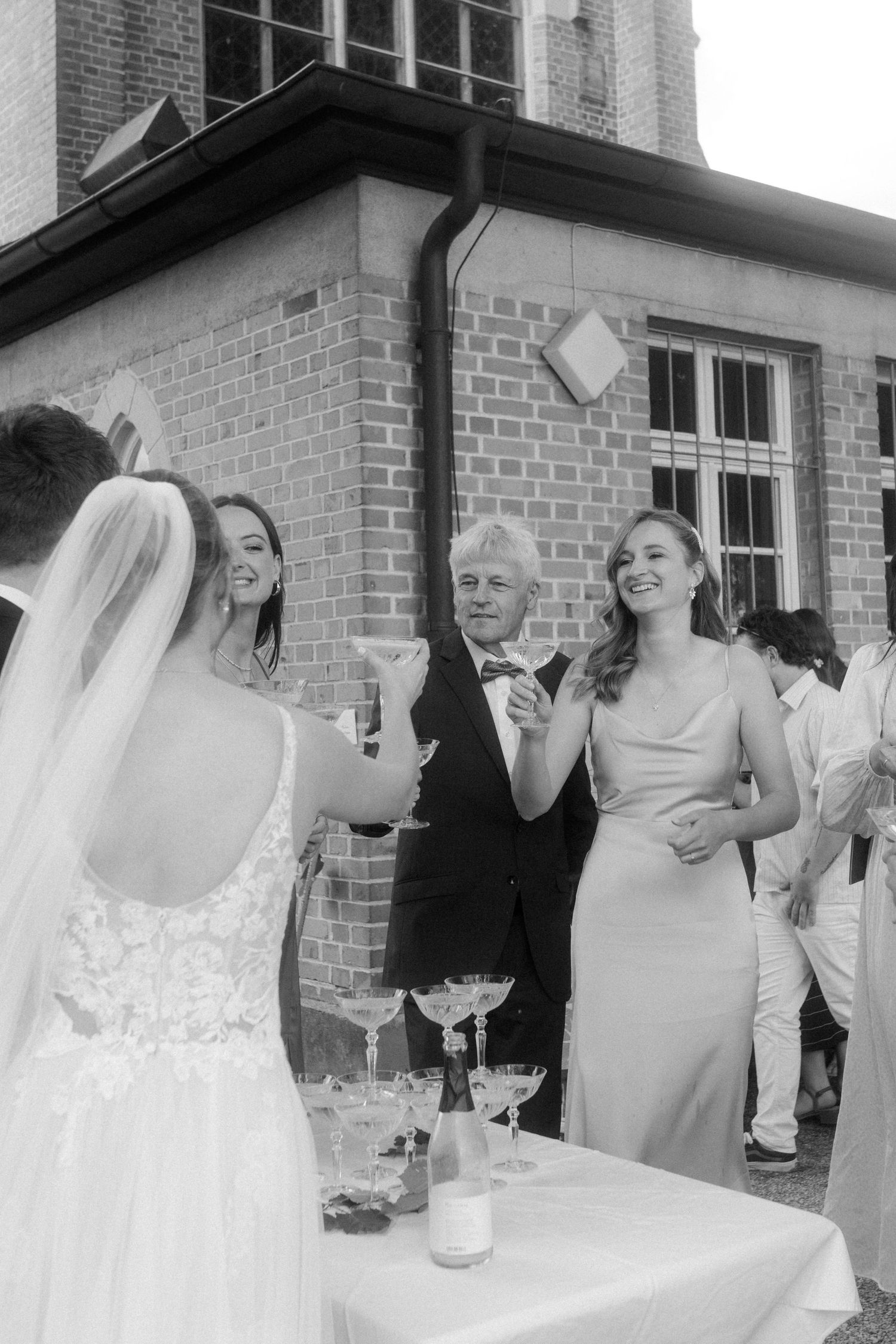 Wedding celebration gathering around champagne tower at brick building venue.