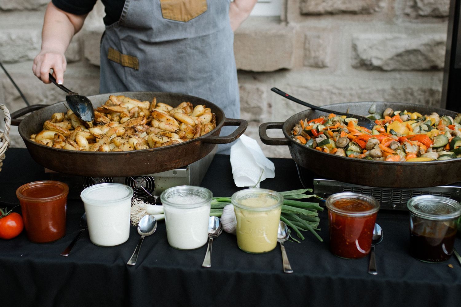 Catering display with sauteed potatoes and various sauces in serving dishes.