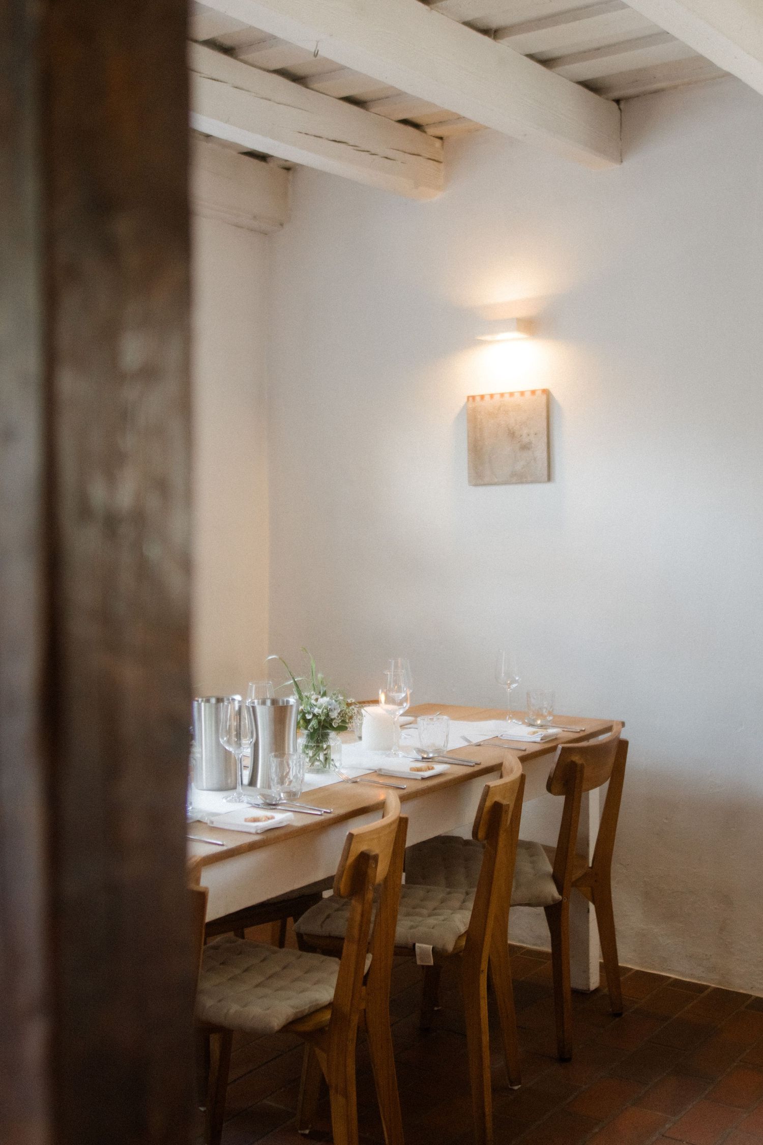 Minimalist white dining room with wooden tables and chairs under exposed beam ceiling.