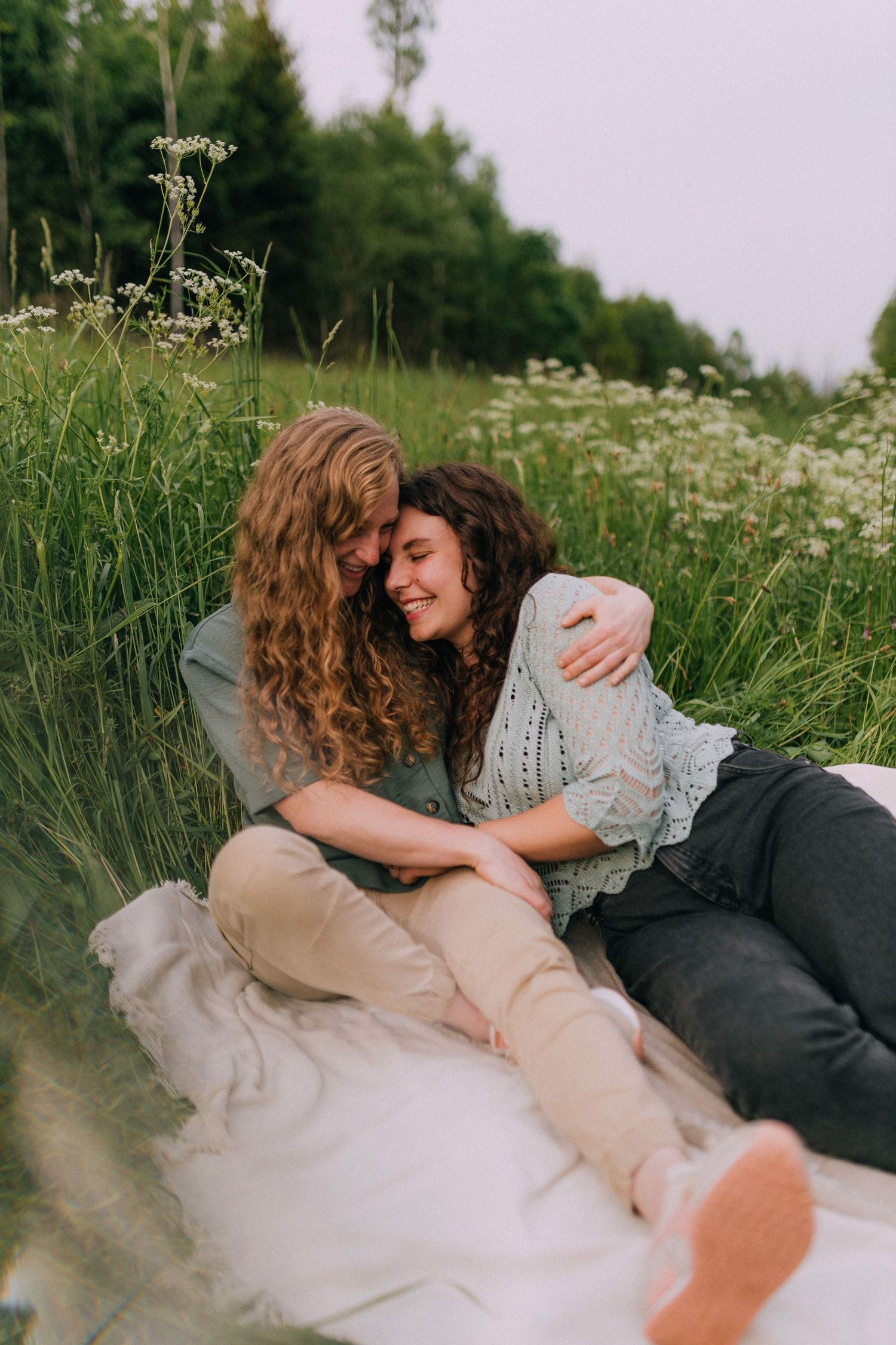 Two people share a tender moment while lying on a blanket in a meadow of flowers.