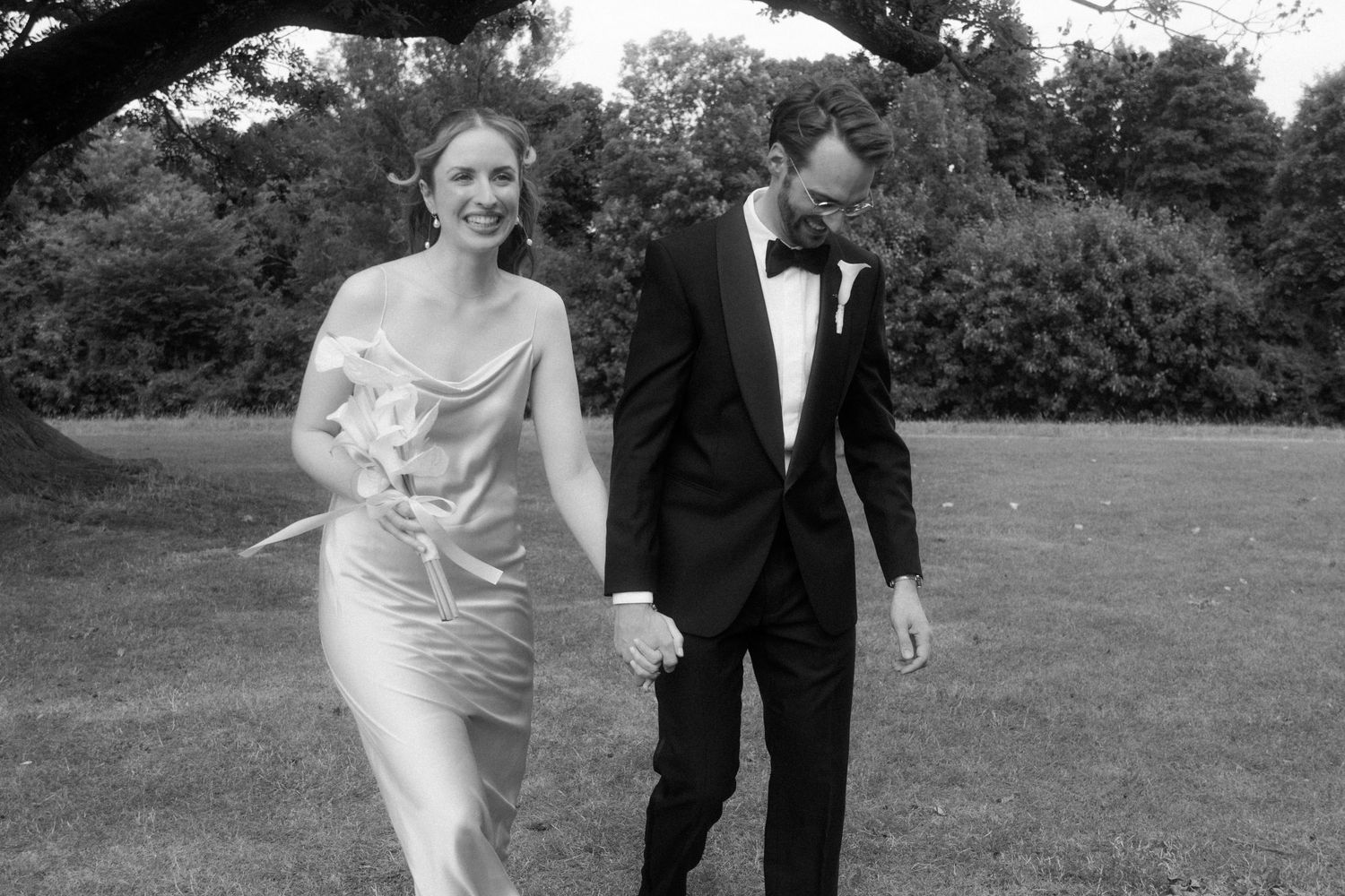 A couple walks hand in hand across a lawn during their wedding day.