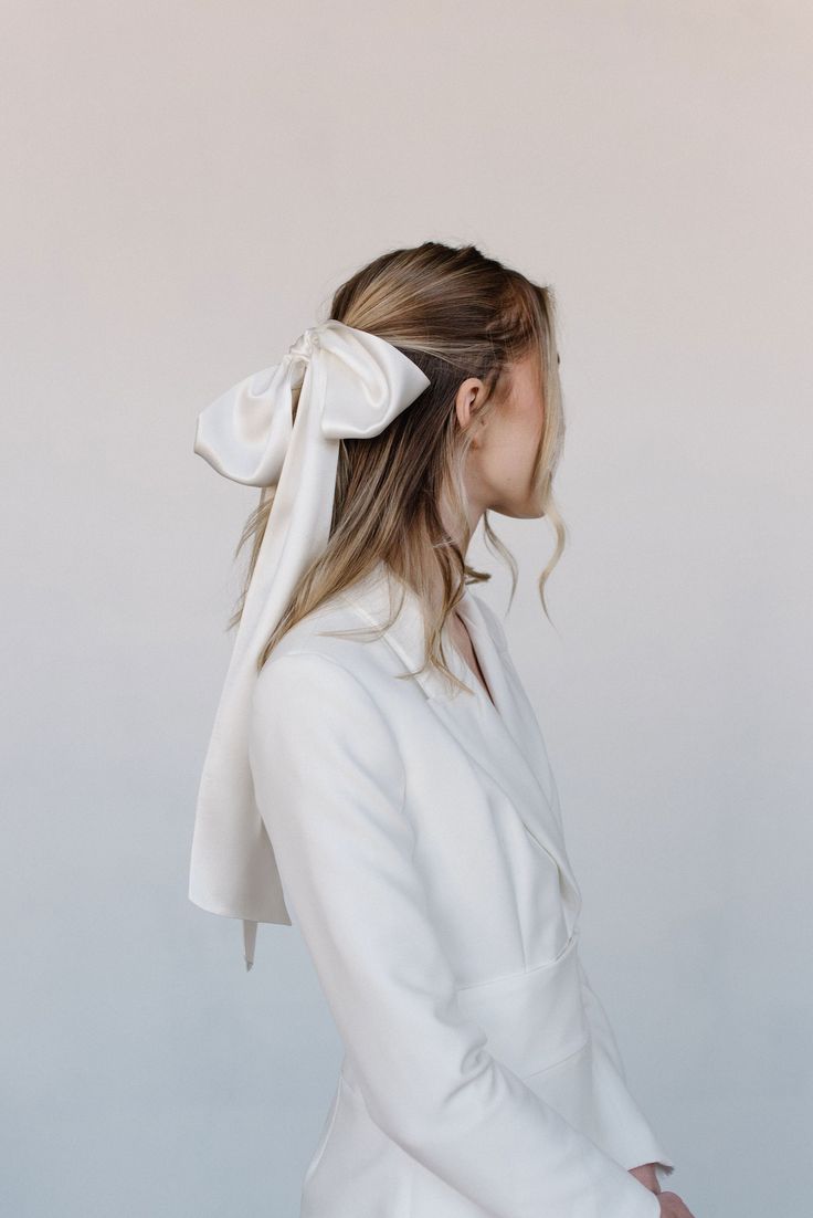 A minimalist white blazer with a large silk bow hair accessory shown in profile.