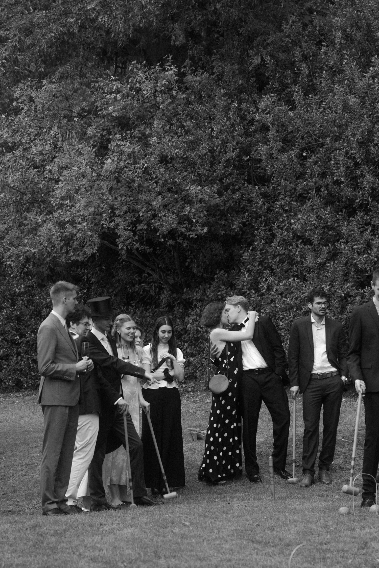 Black and white photo of wedding guests playing croquet on a lawn.