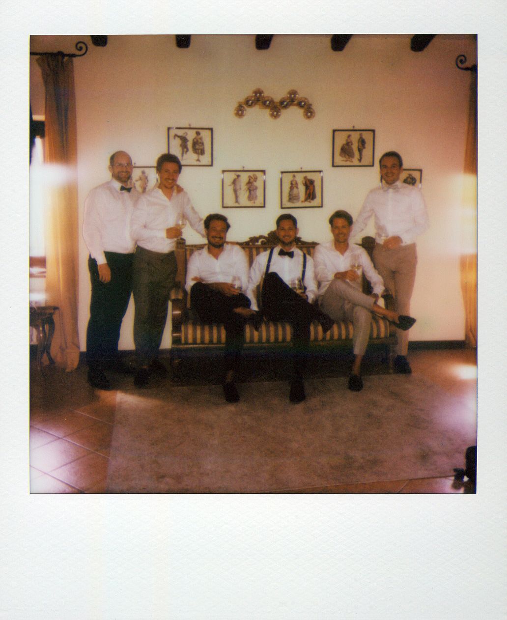 A group in formal attire sits on wooden benches against a wall with framed artwork.