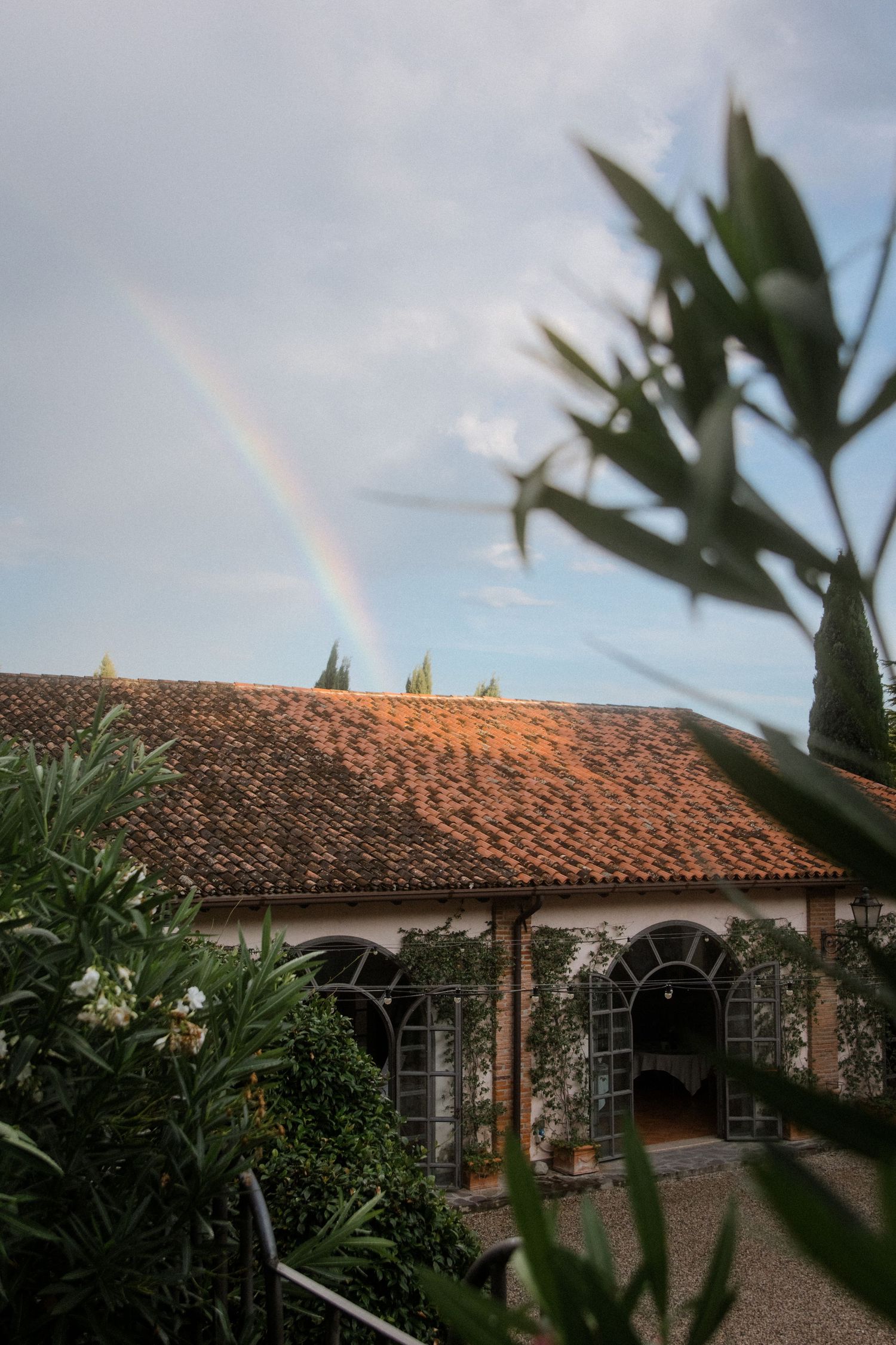 Mediterranean villa with terracotta roof and arched windows under a rainbow in the evening sky.