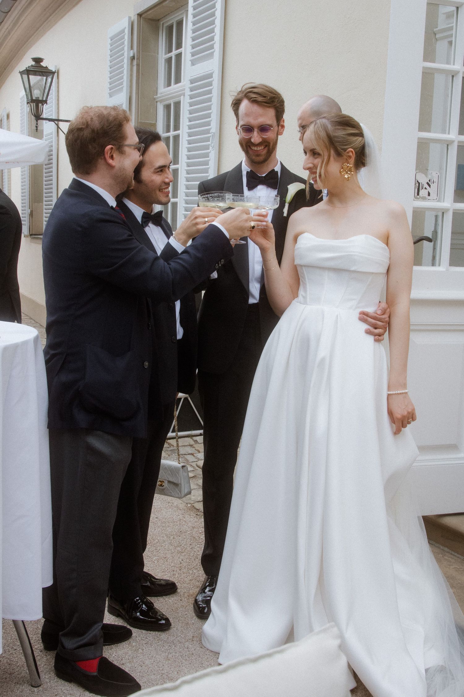 Wedding guests toasting and celebrating outside a white building with shutters.