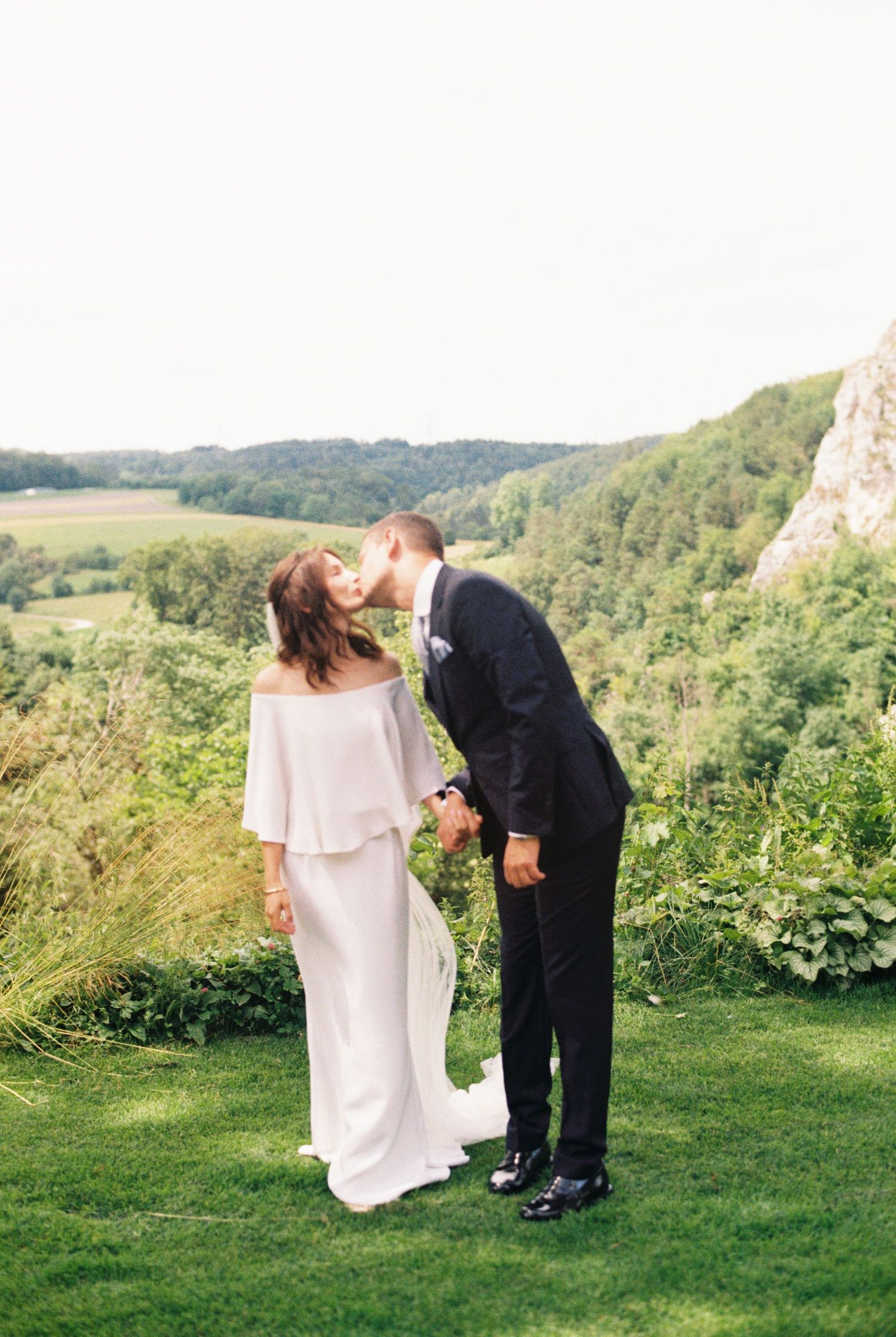 A wedding couple shares a tender moment on a hilltop overlooking a scenic valley landscape.