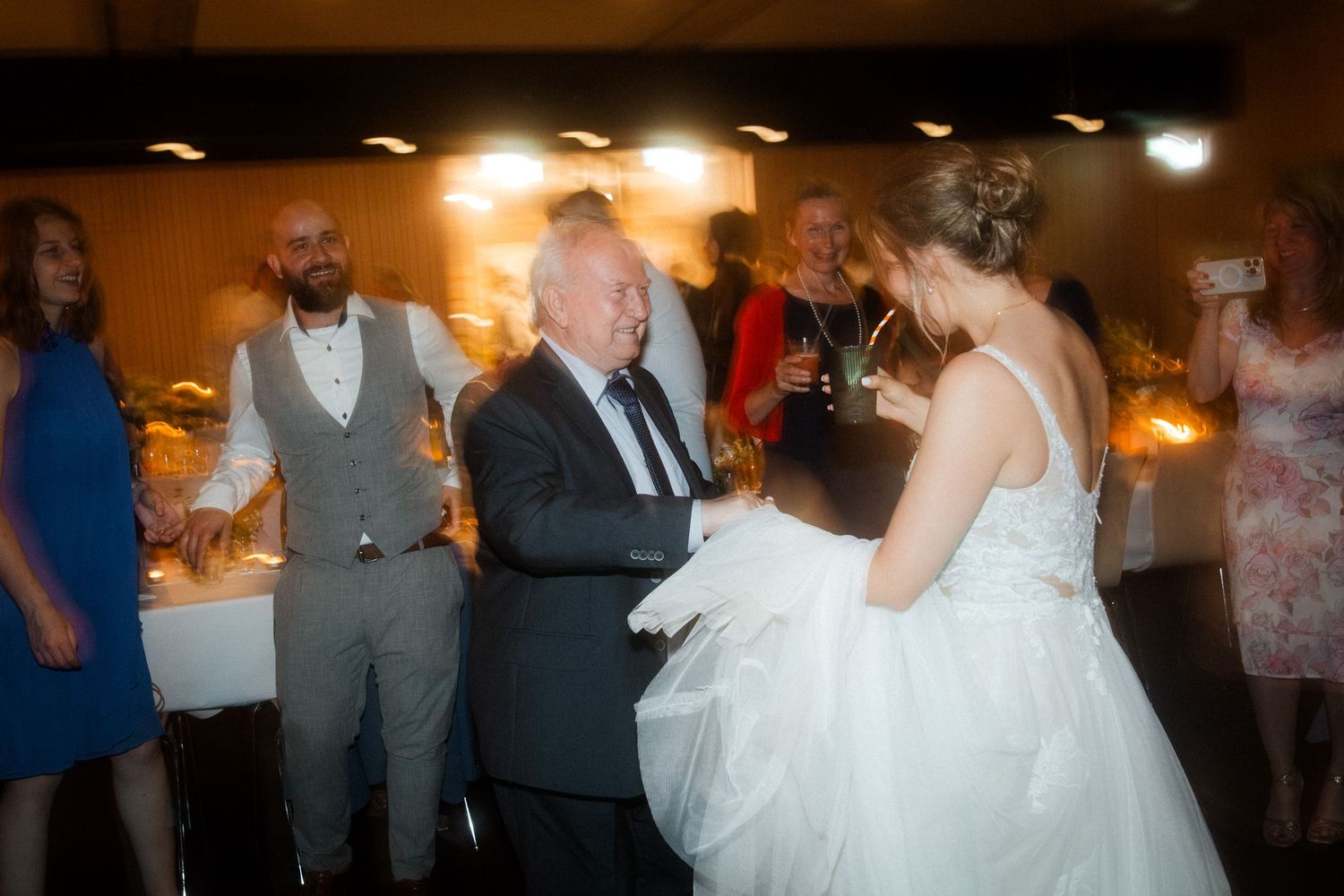 Wedding guests dancing with bride in white gown during reception celebration.