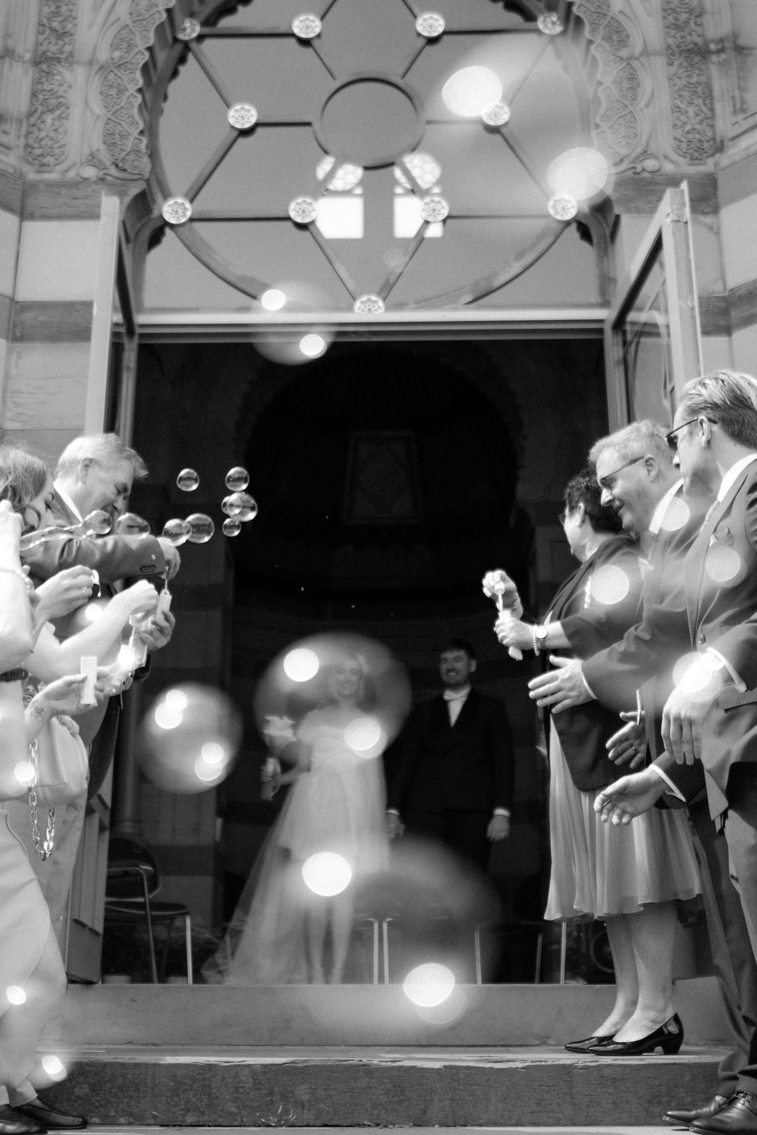 Vintage-style black and white photo of guests blowing bubbles at a wedding ceremony.