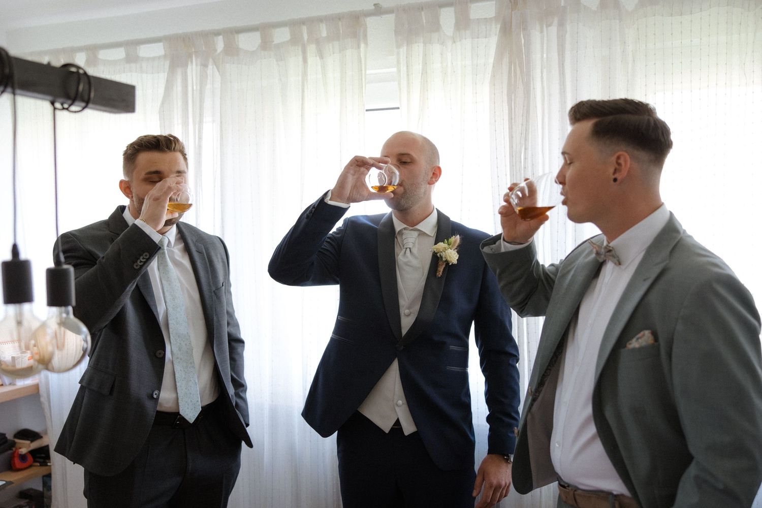 Wedding party members in suits enjoying celebratory drinks together.