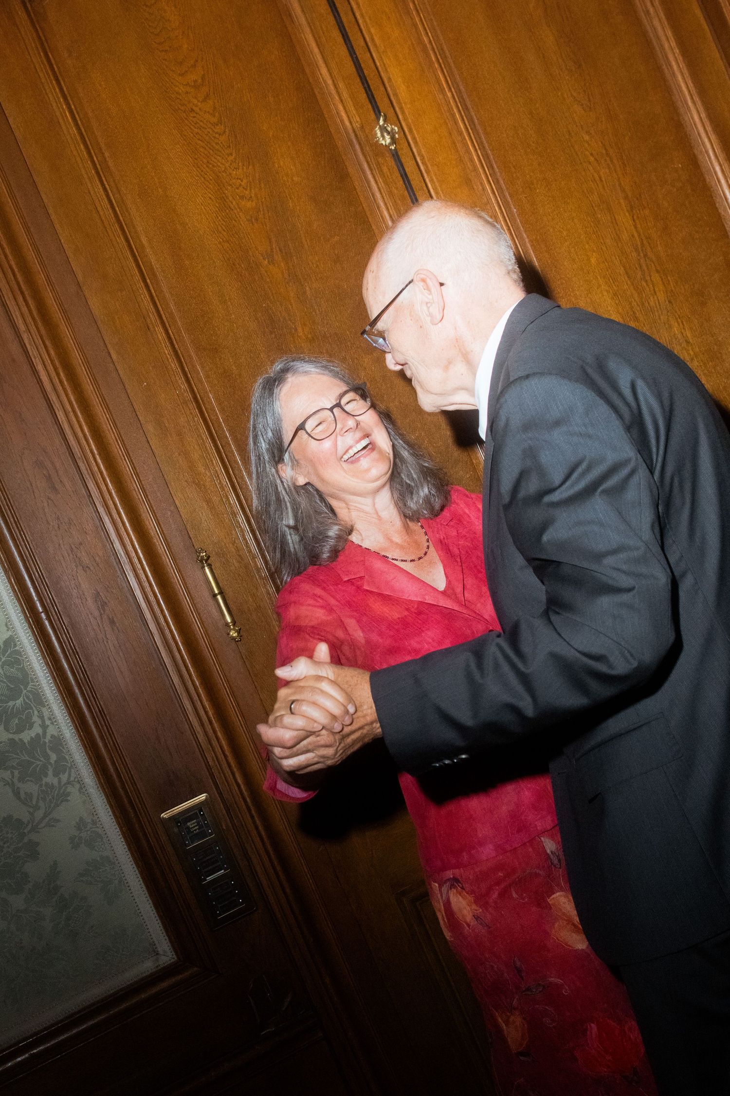 Couple dancing and smiling together against wooden paneled wall at formal event.