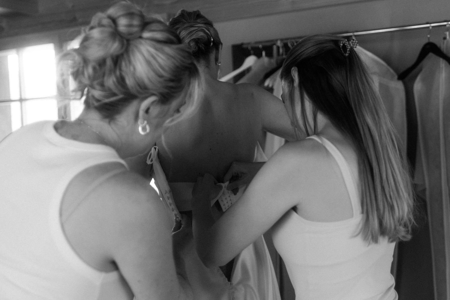 Two women in white tops looking through a clothing rack in a black and white photo.