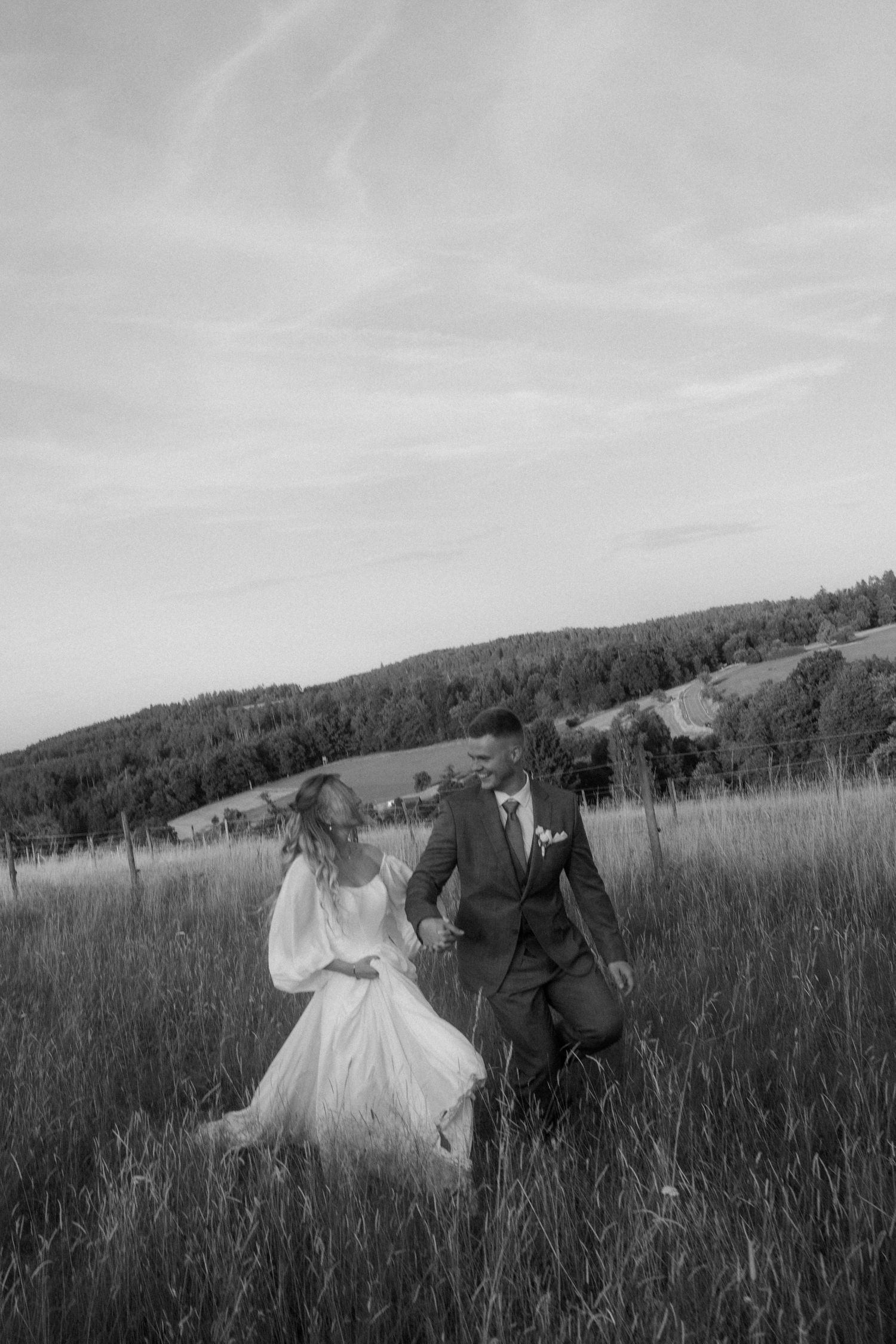 Black and white photo of couple walking through tall grass in a meadow.