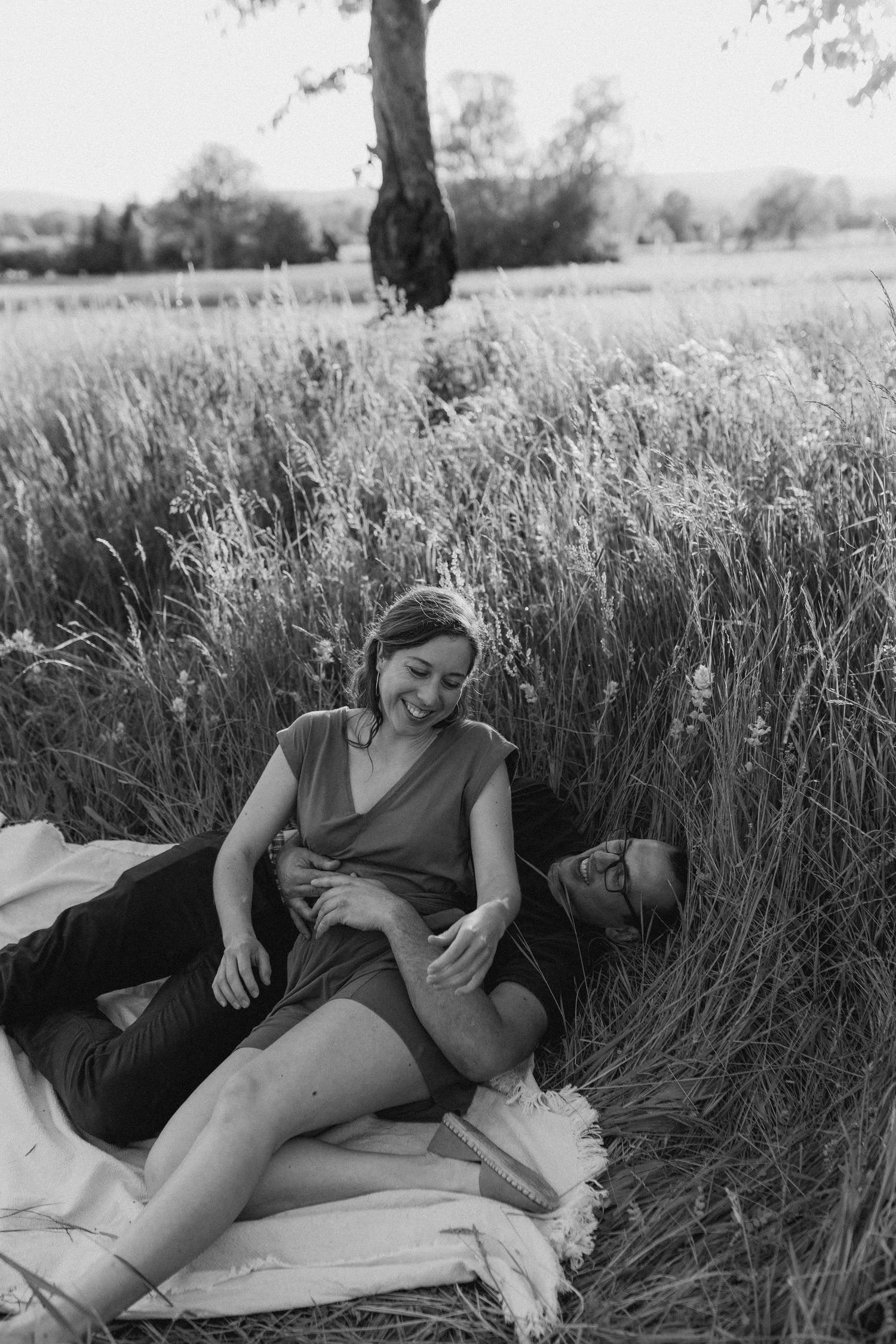 Couple relaxing on a blanket in tall grass during an outdoor photoshoot.