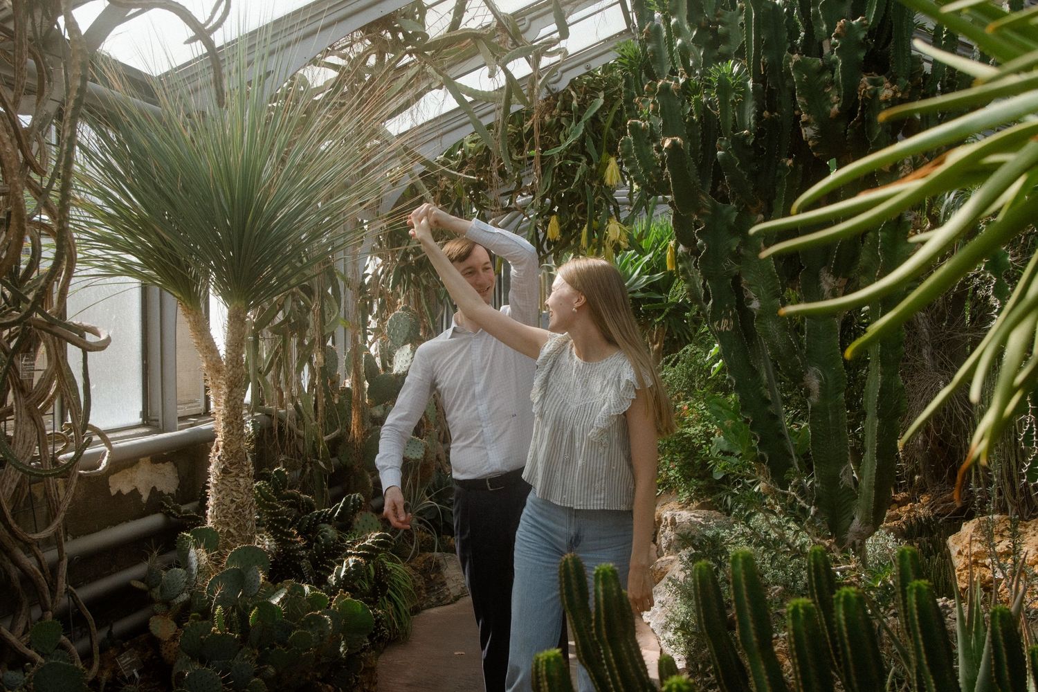 Couples enjoying a romantic moment in a sunlit conservatory filled with exotic plants.