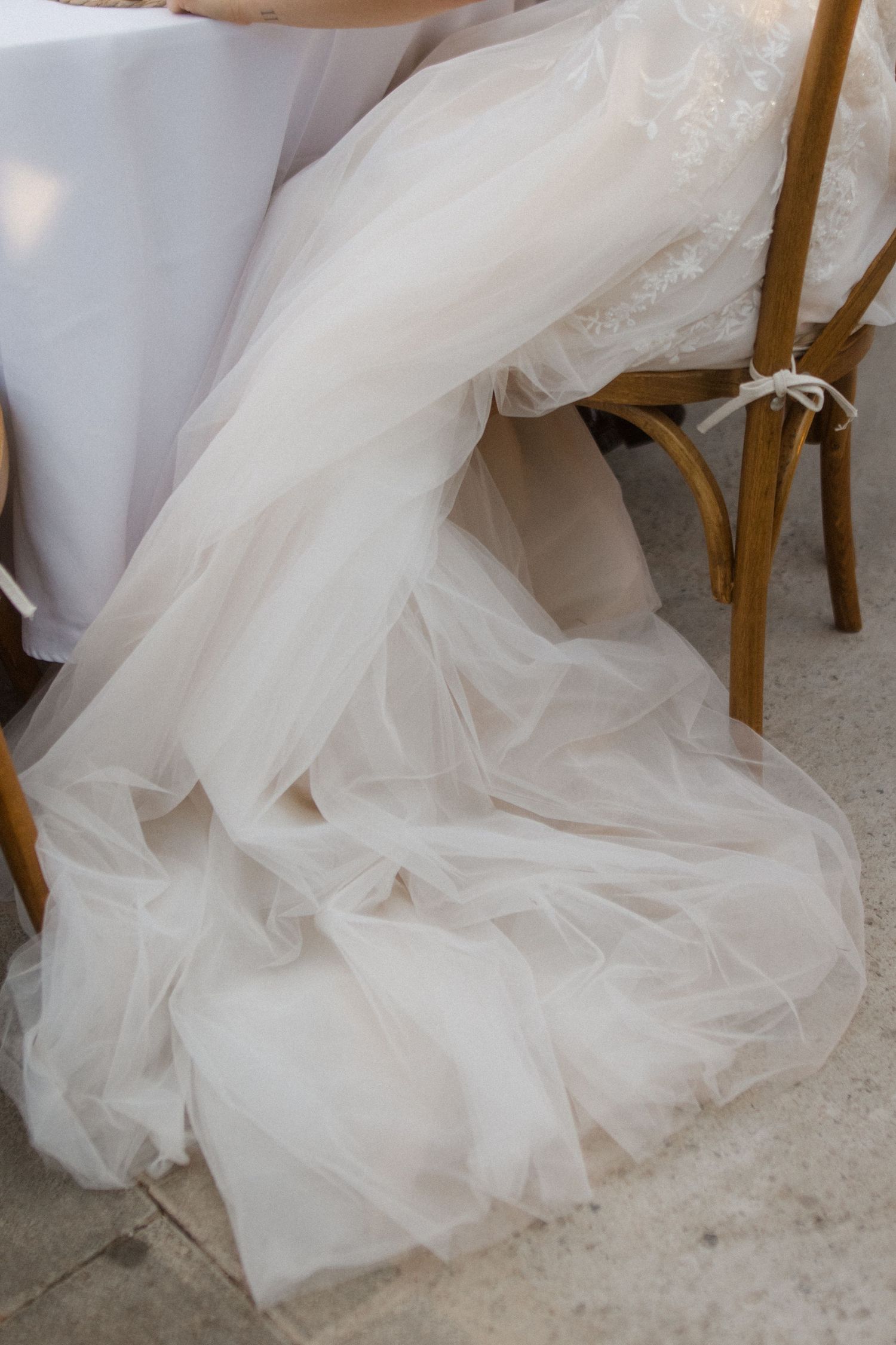 Flowing white tulle wedding dress detail draped over wooden chair.