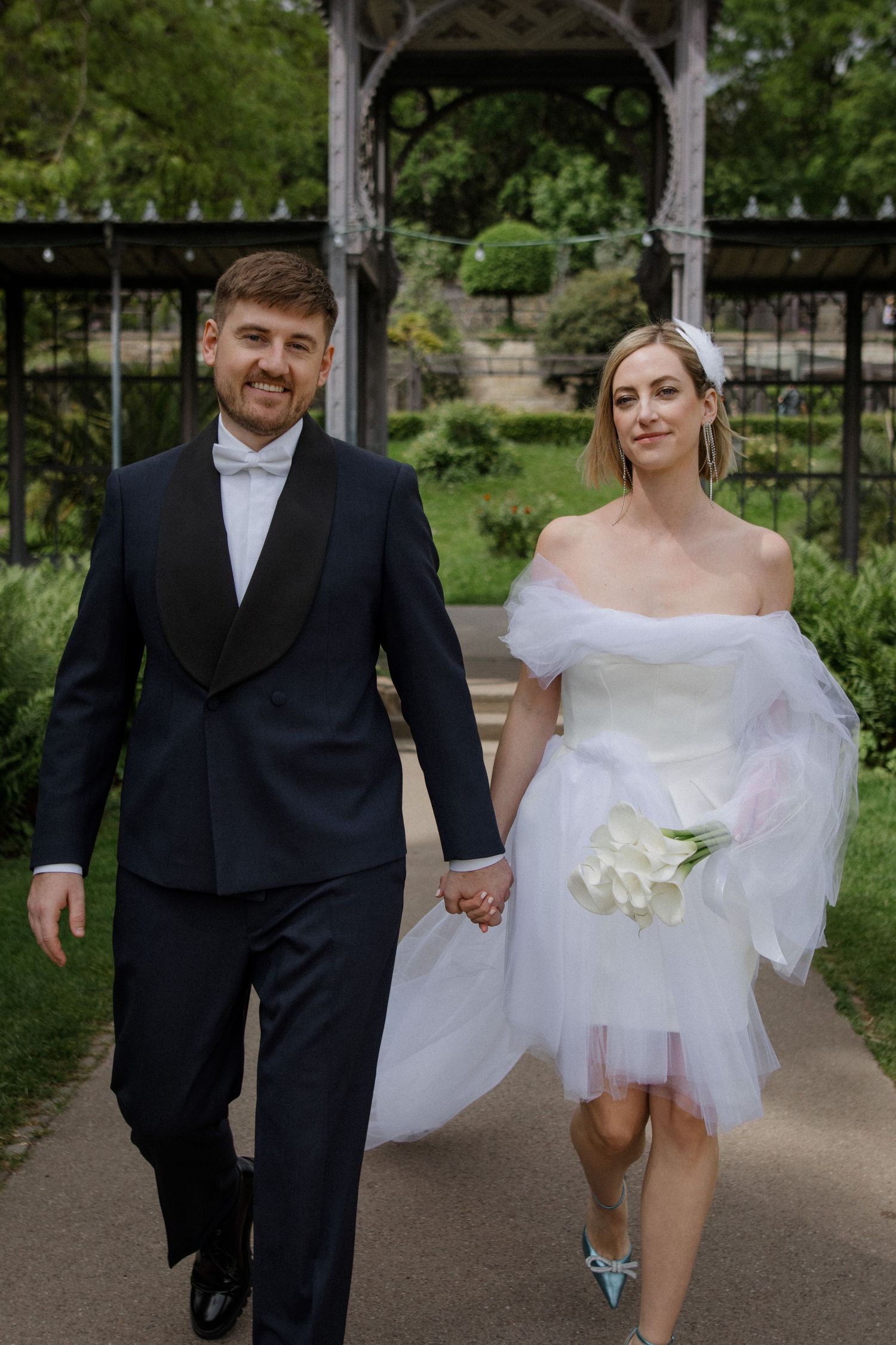 Bride and groom holding hands while walking through garden archway.