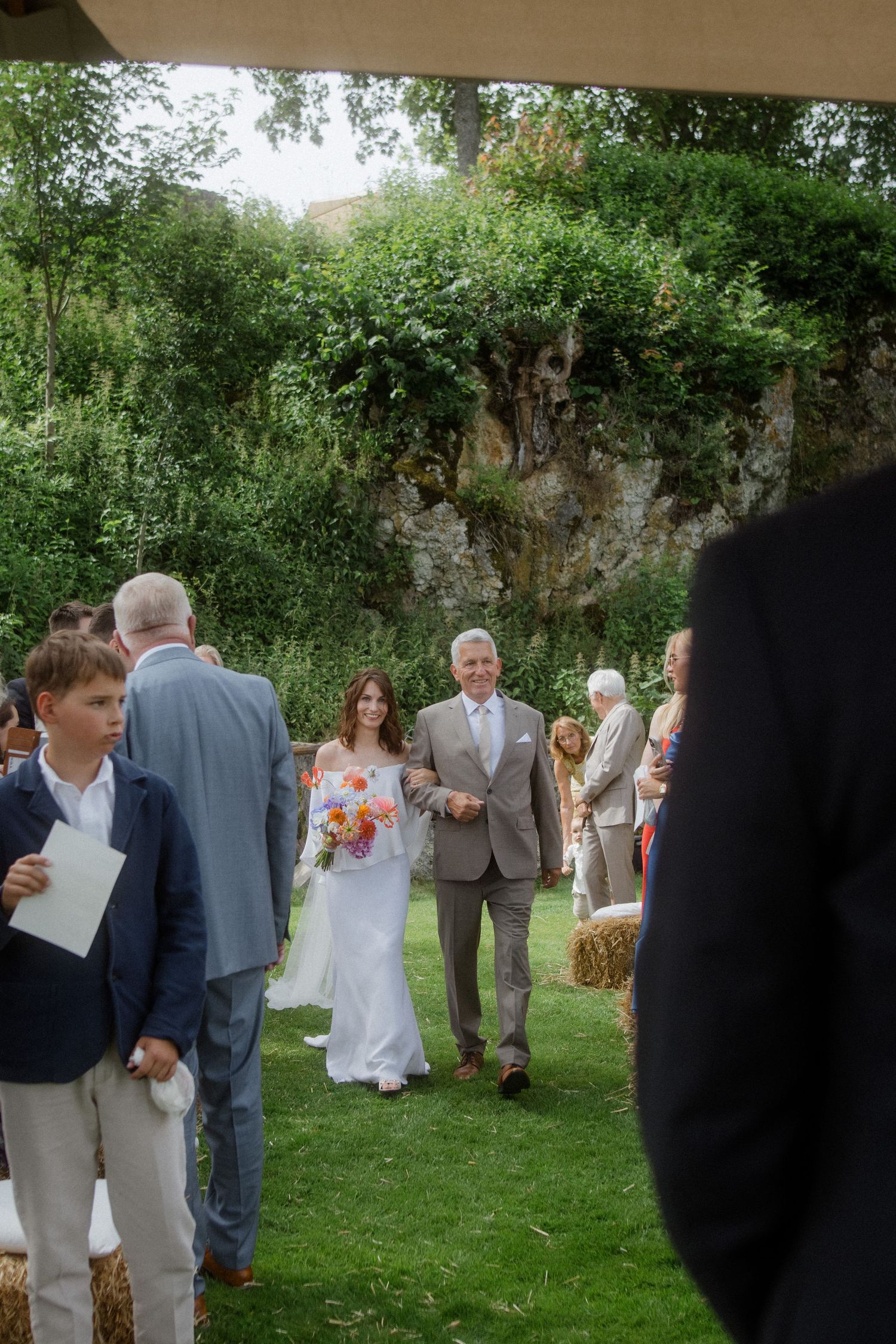 Outdoor wedding gathering with guests mingling on lawn near stone walls.
