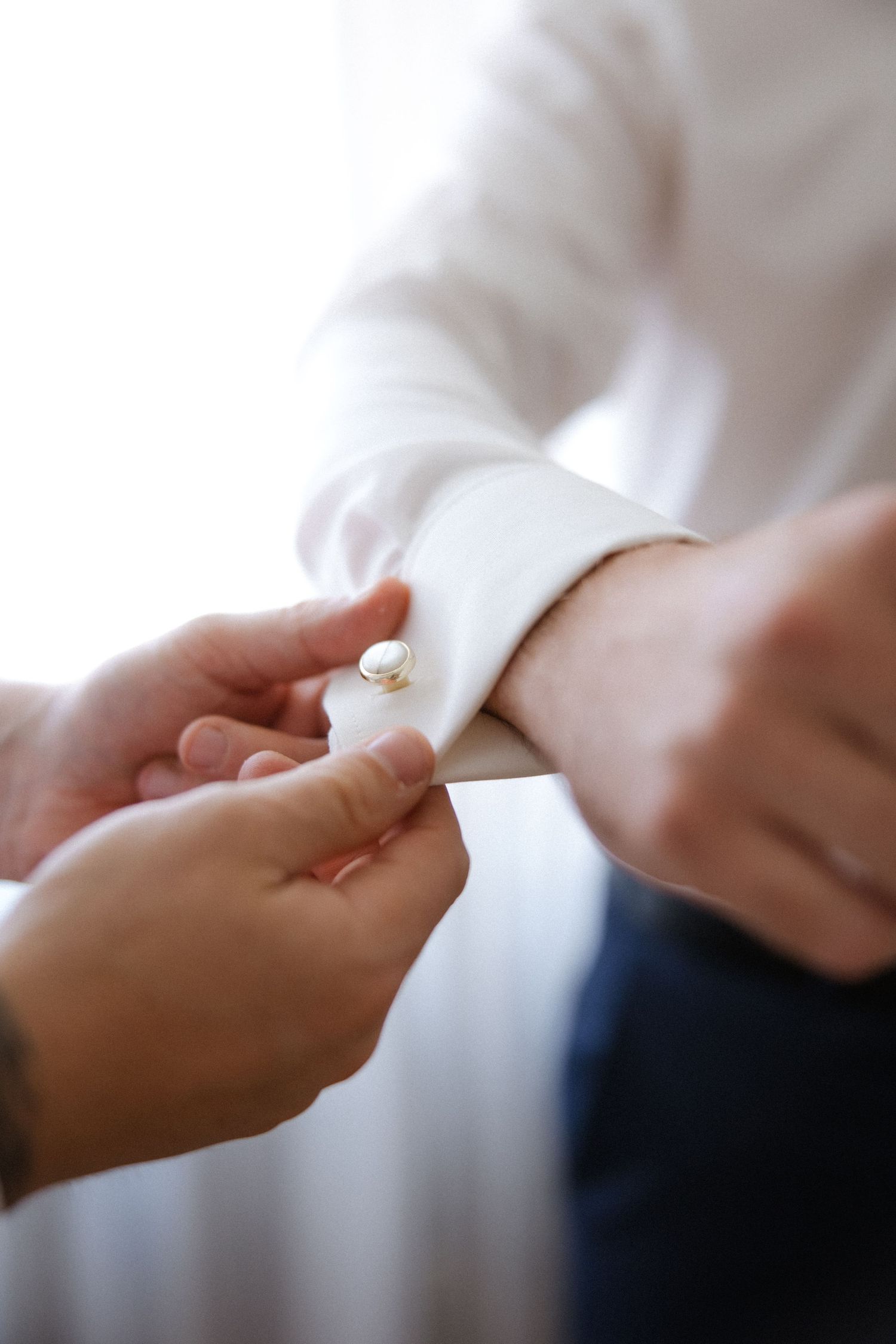 Close-up of hands fastening a cufflink on a white dress shirt sleeve.