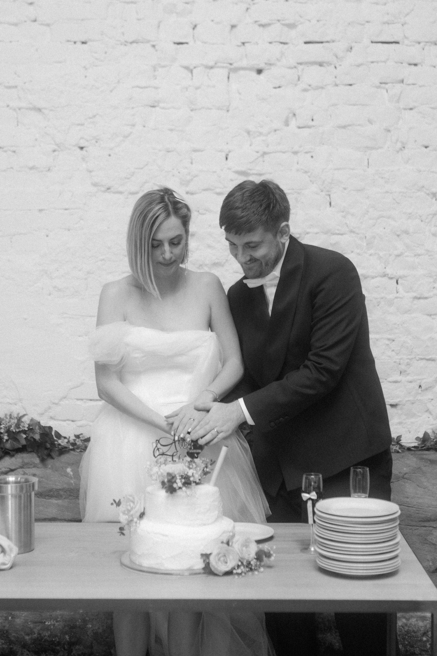 A black and white photo of newlyweds cutting their wedding cake together.