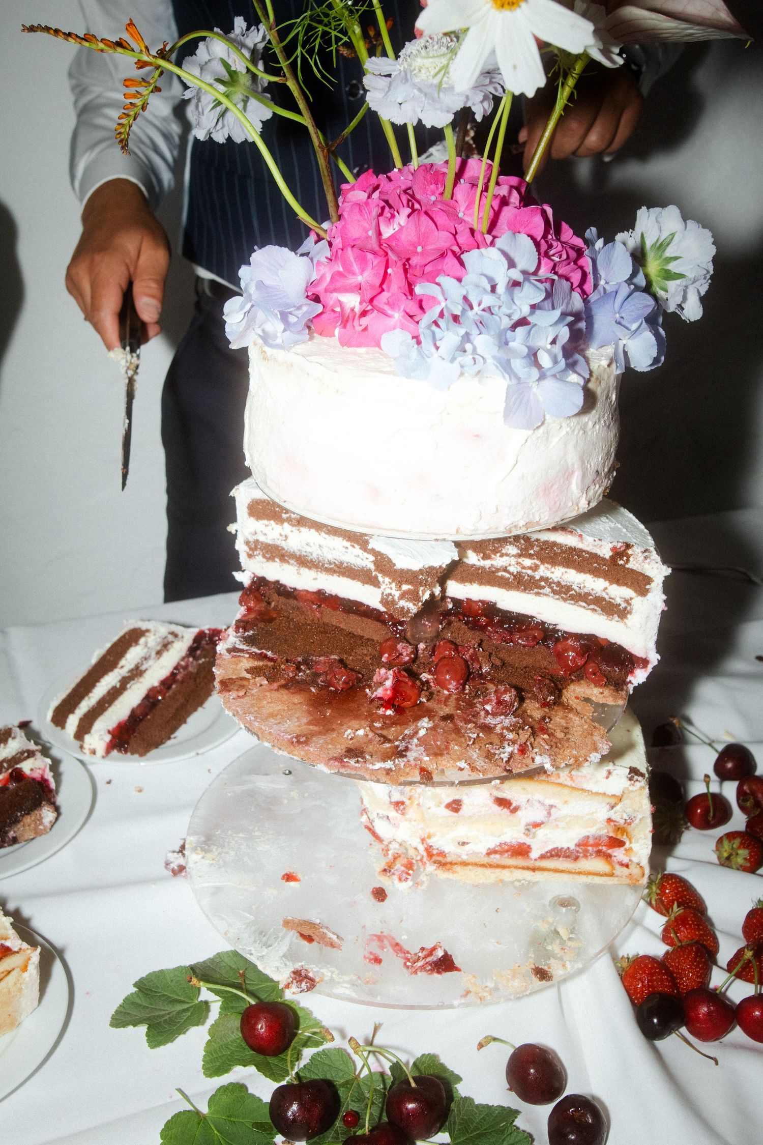 A sliced wedding cake reveals chocolate layers decorated with fresh flowers and cherries.