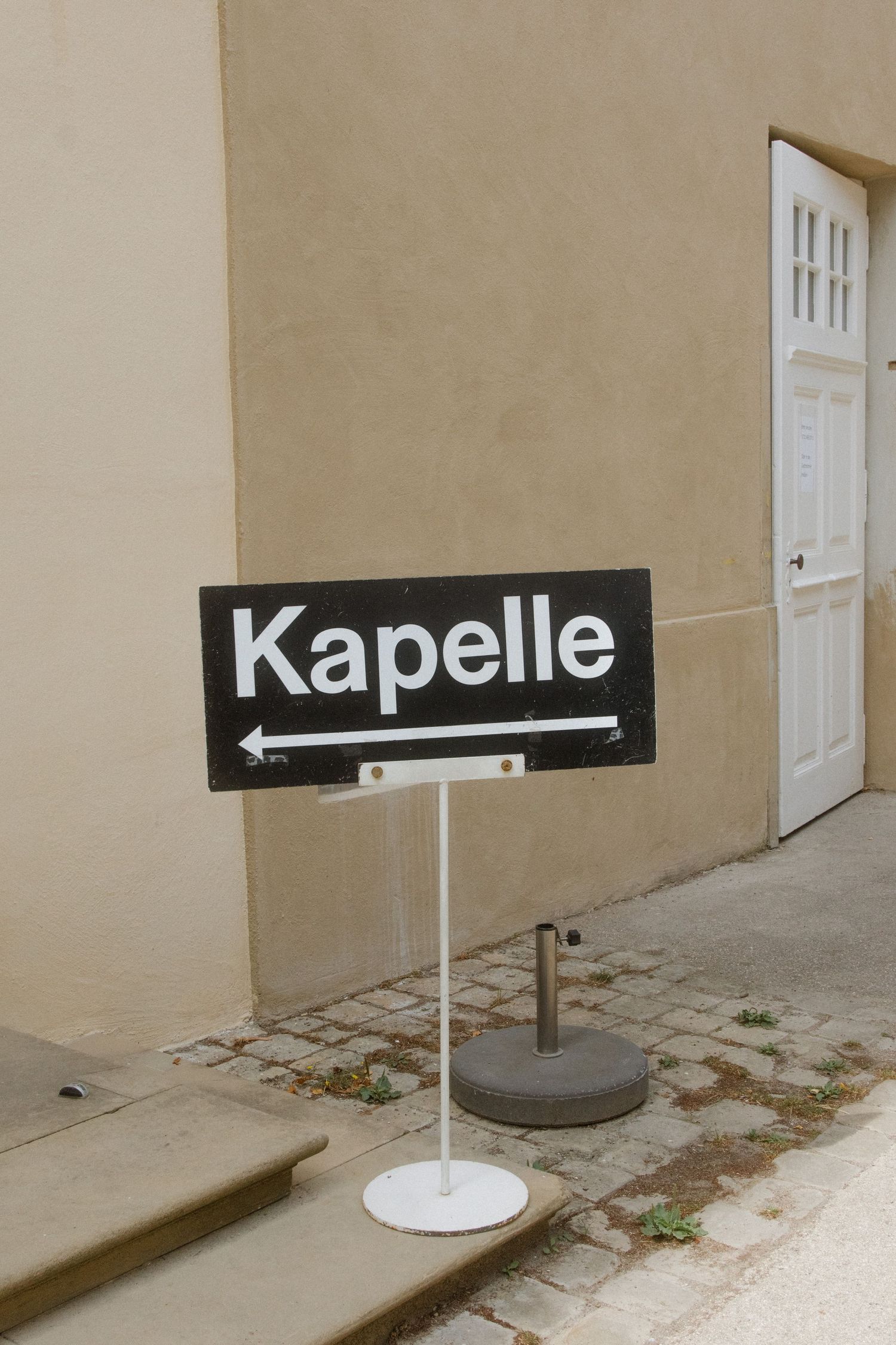 A black and white directional sign reading 'Kapelle' mounted on a beige wall.