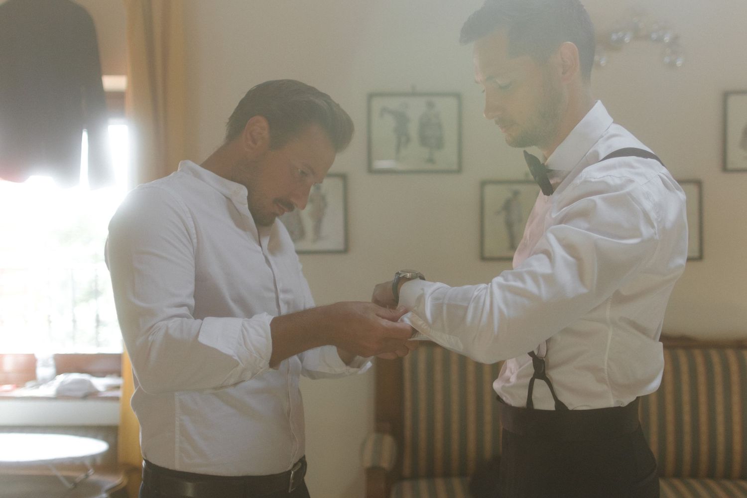 Two people in formal attire prepare for an event in a room with framed artwork on the walls.