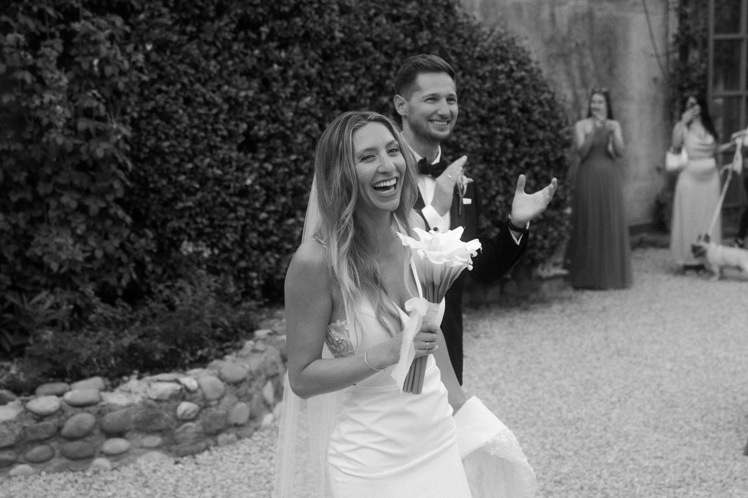 Wedding guests dance and celebrate on a gravel courtyard surrounded by cypress trees and string lights.