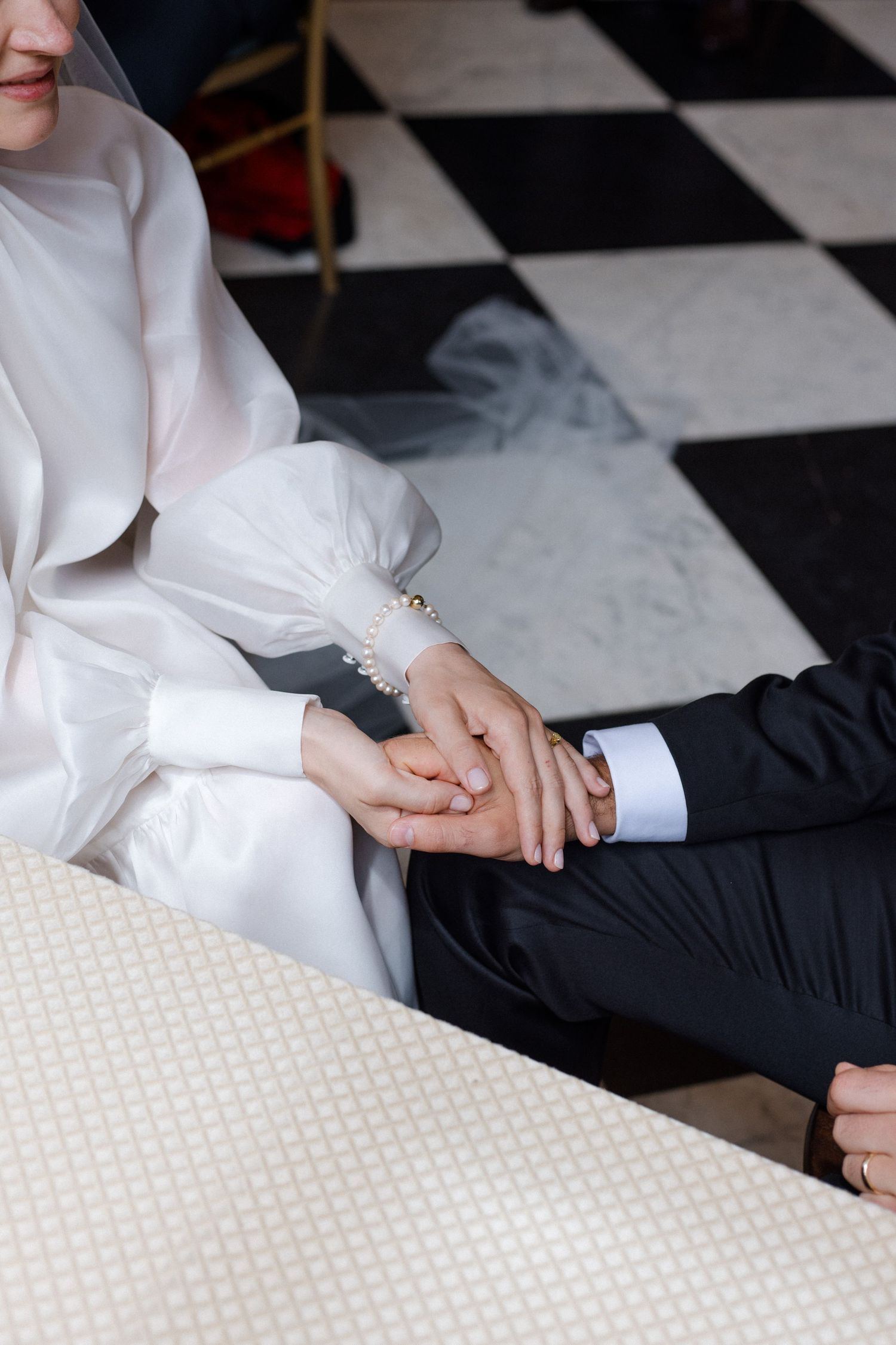 Bride in white wedding dress and groom in black suit holding hands on checkered floor.