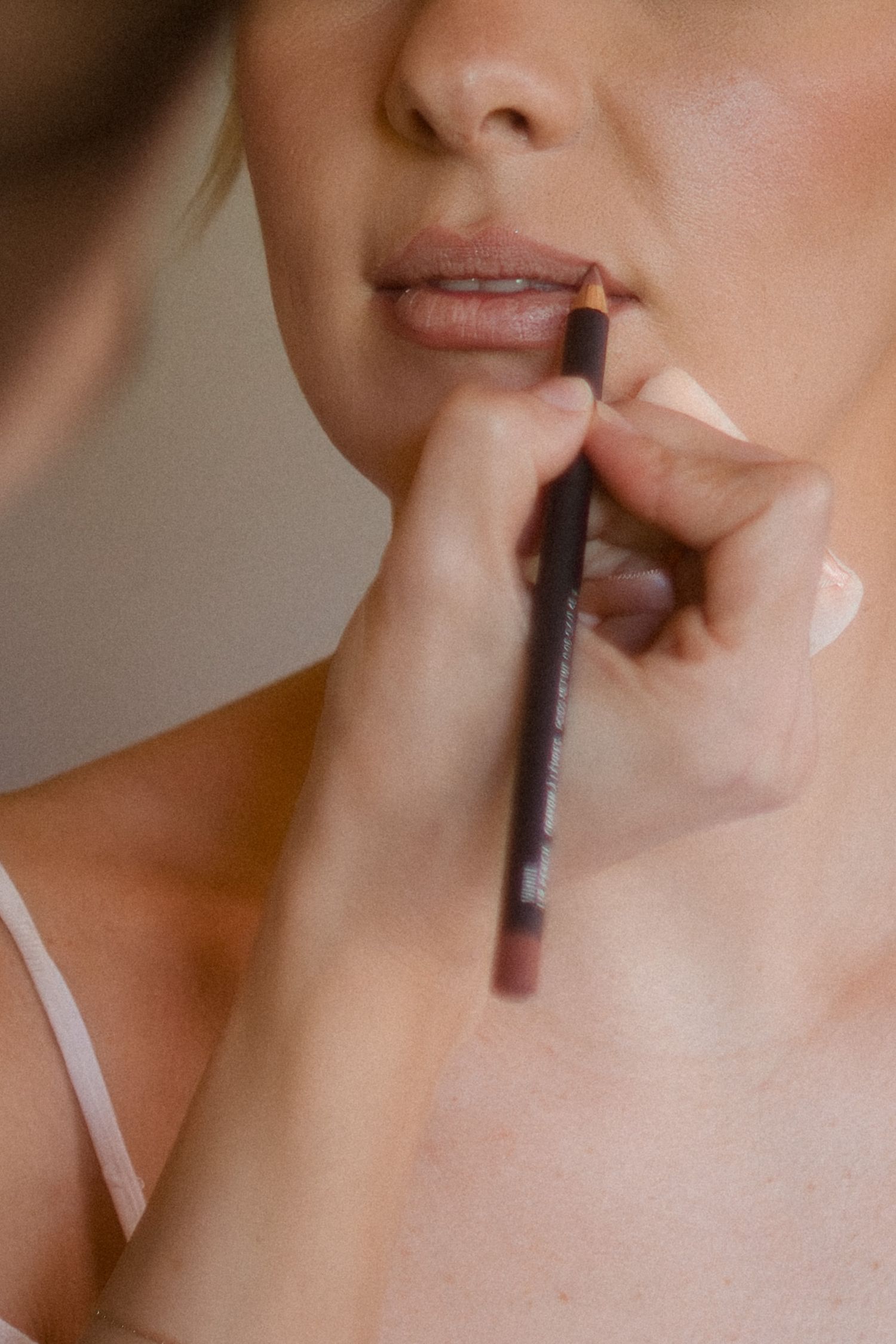 A makeup artist applying dark lip liner pencil to a woman's lips for precise definition.