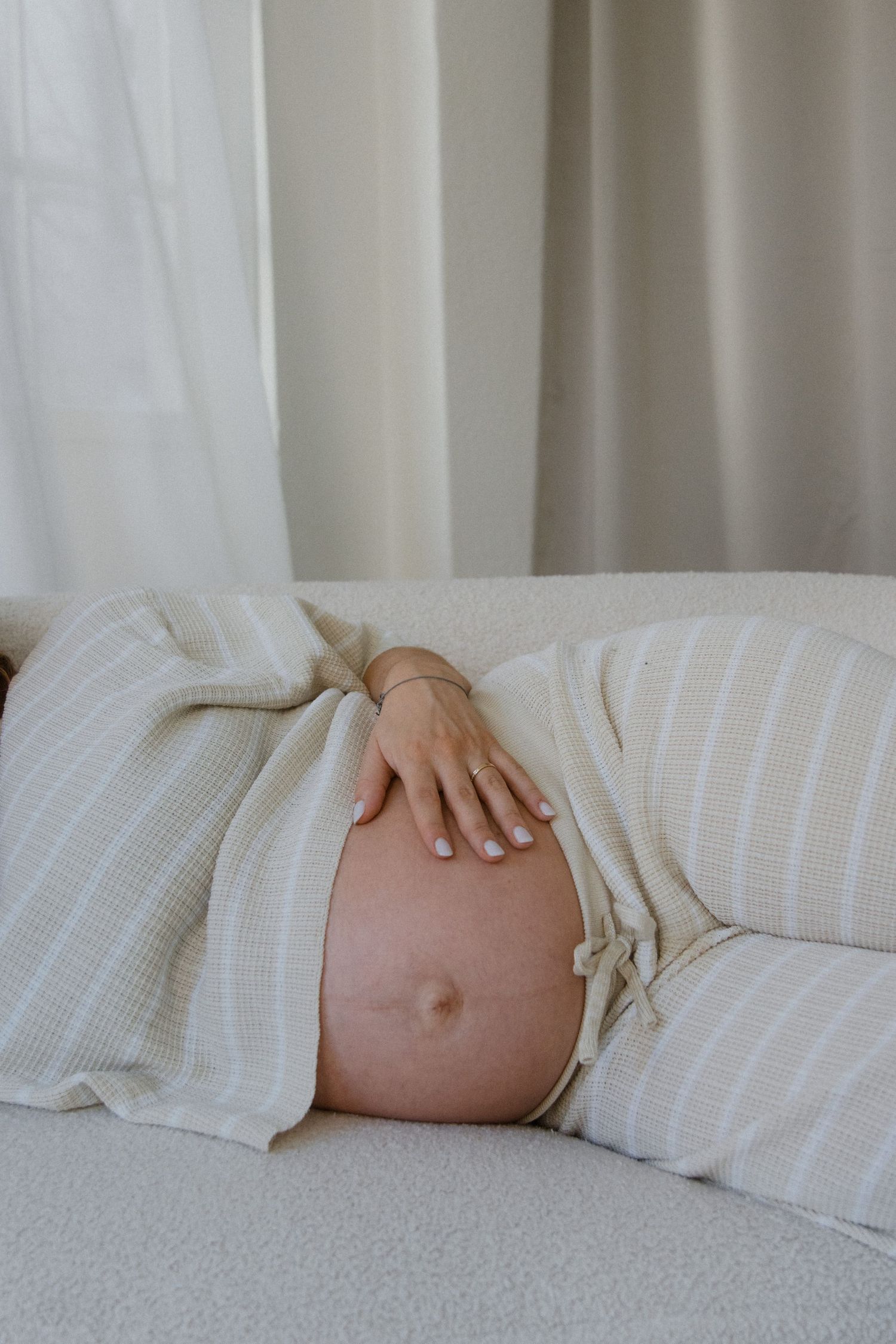 Close-up of a pregnant belly covered with white striped fabric on a bed.