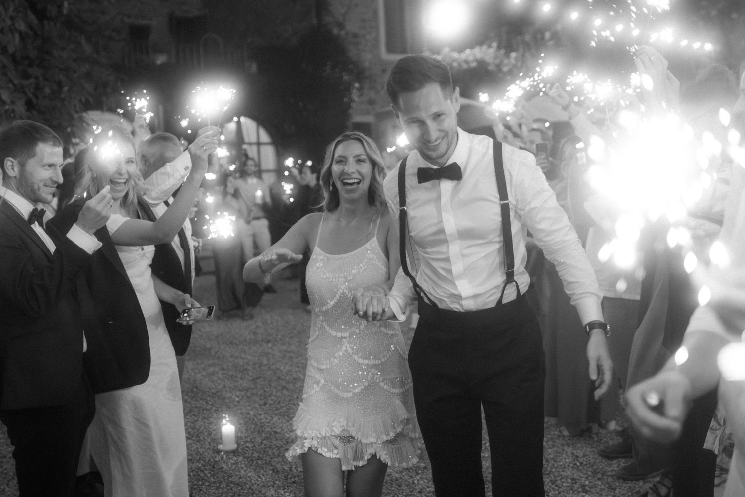 Black and white photo of bride and groom walking through sparkler tunnel at outdoor wedding reception.
