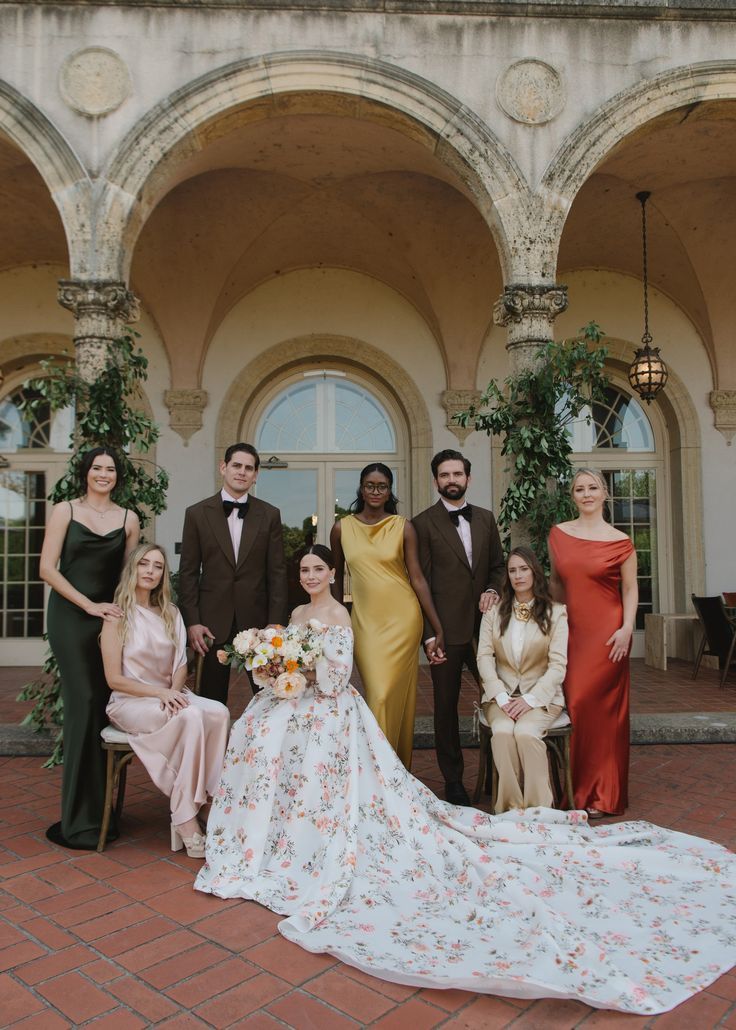 Wedding party poses under elegant archways with bride in floral gown and bridesmaids in jewel-toned dresses.