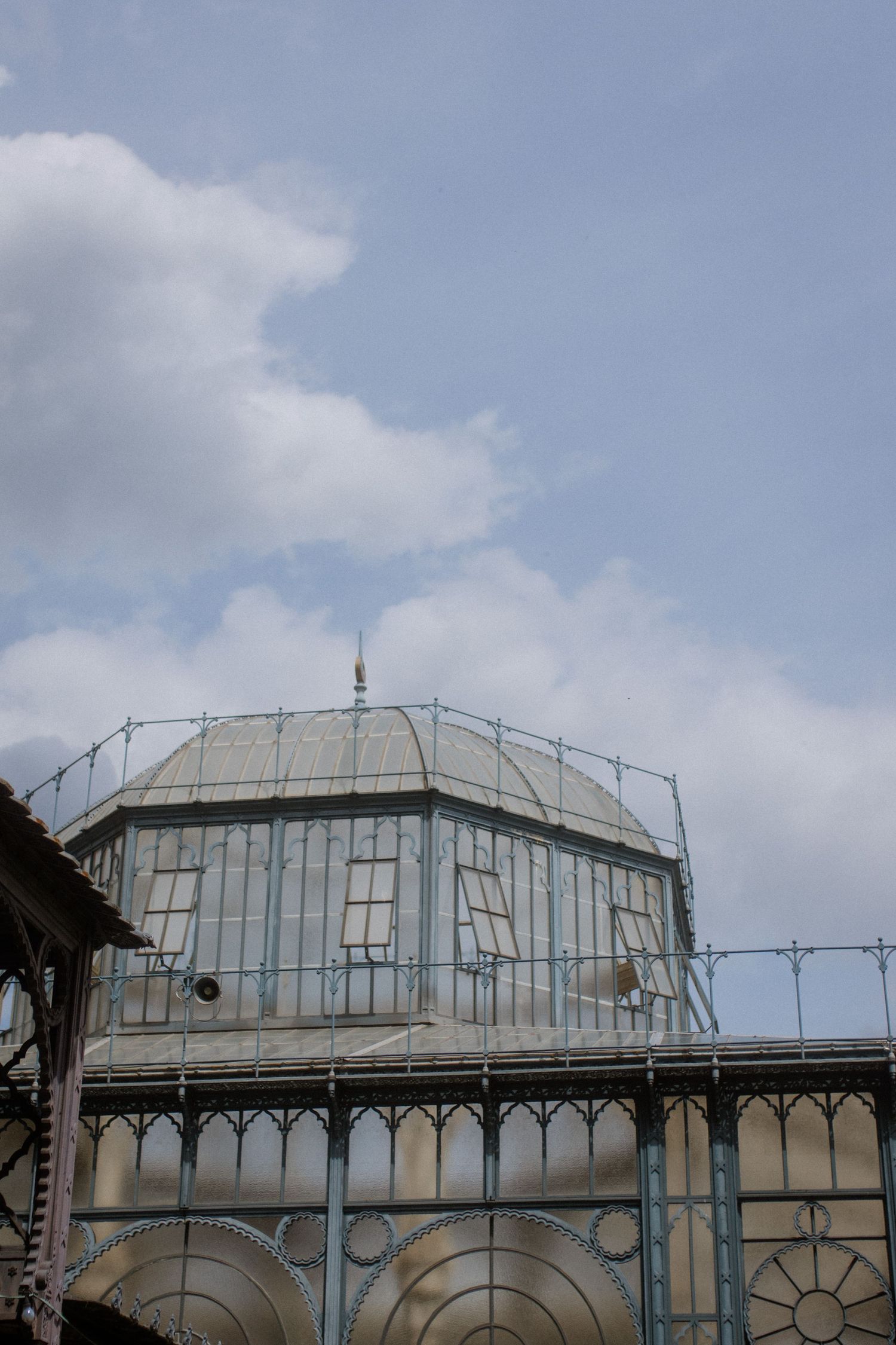 Architectural detail of a glass conservatory dome with ornate metalwork against cloudy sky.