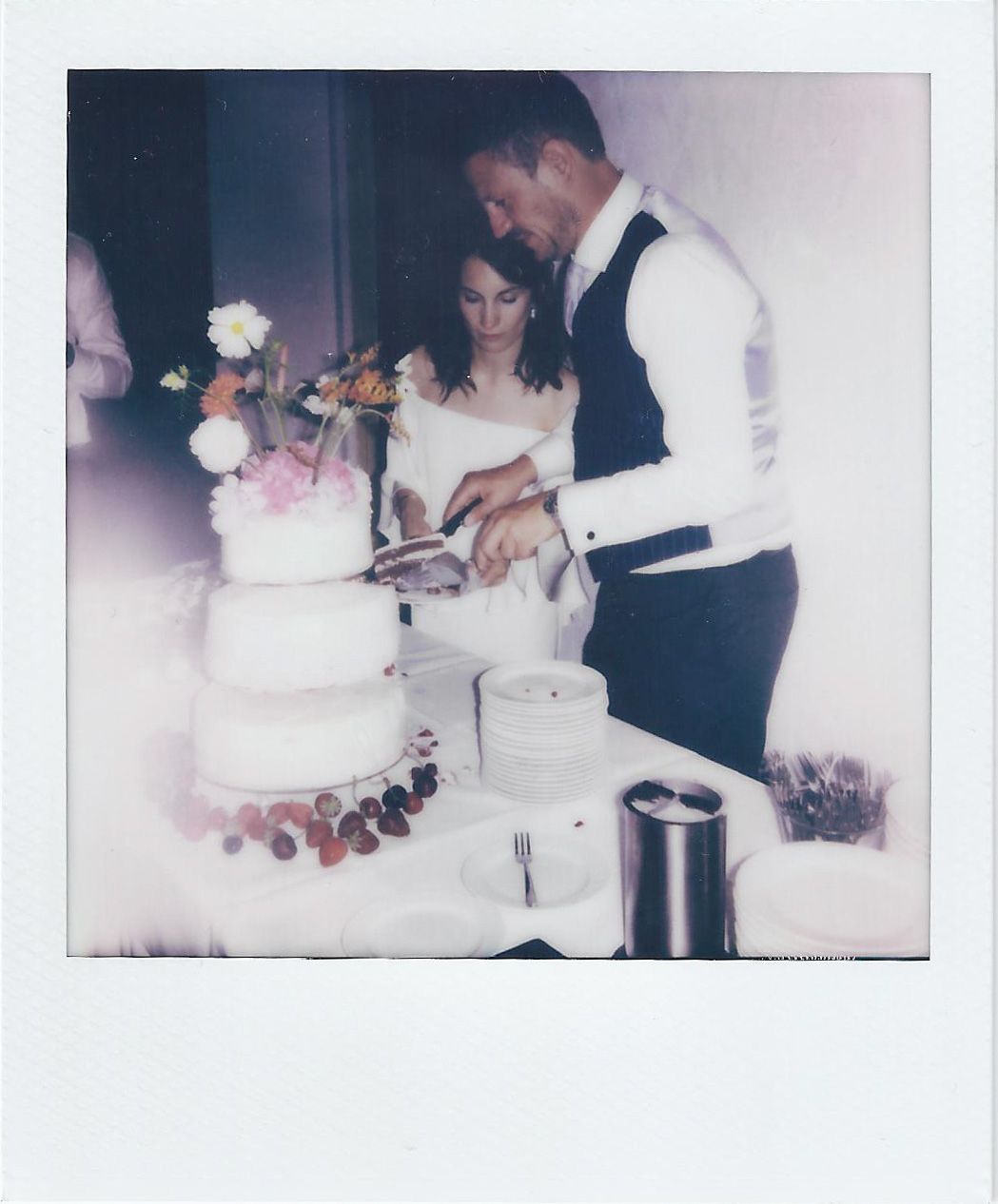A couple cuts into their multi-tiered white wedding cake during the reception.