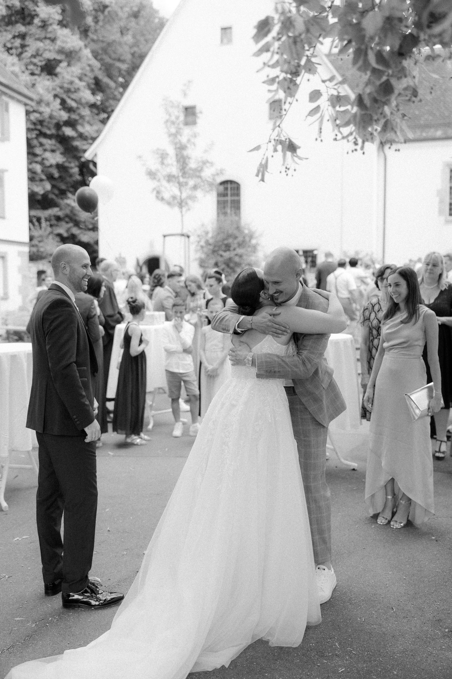 A black and white photo captures an embrace between guests at an outdoor wedding celebration.