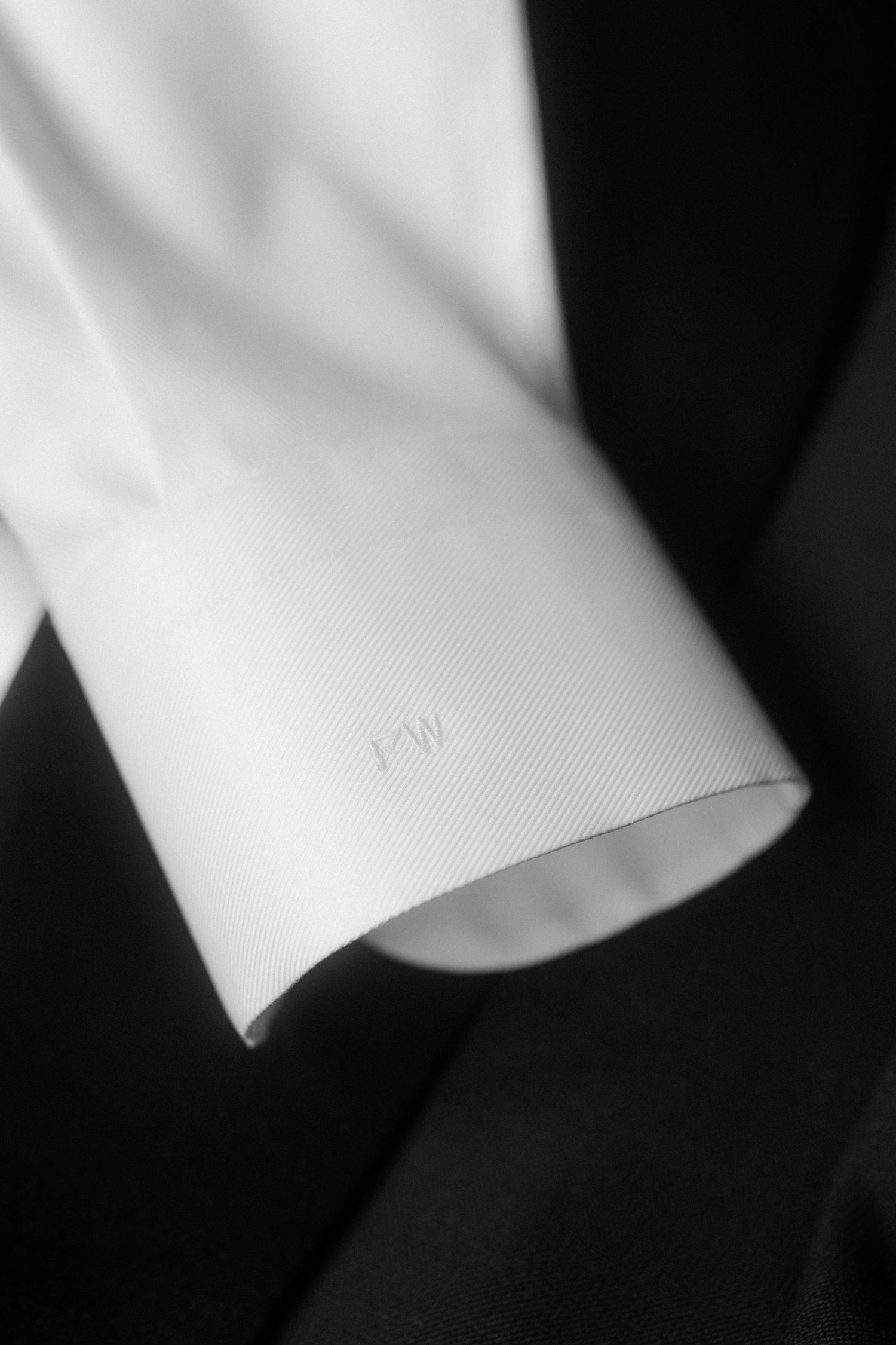 Close-up view of a white shirt cuff with subtle monogram stitching.