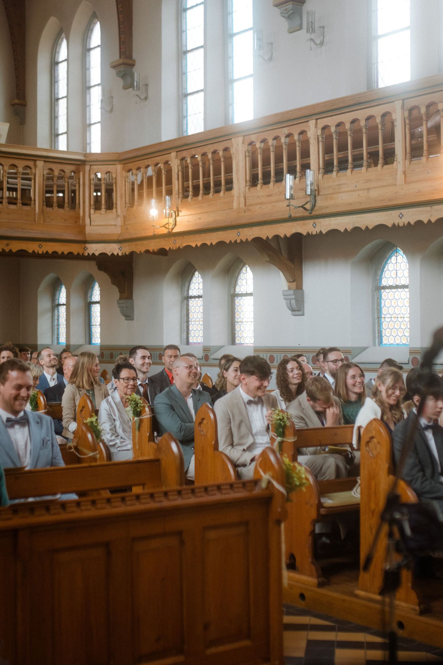 Church pews filled with wedding guests beneath ornate wooden balconies and arched windows.