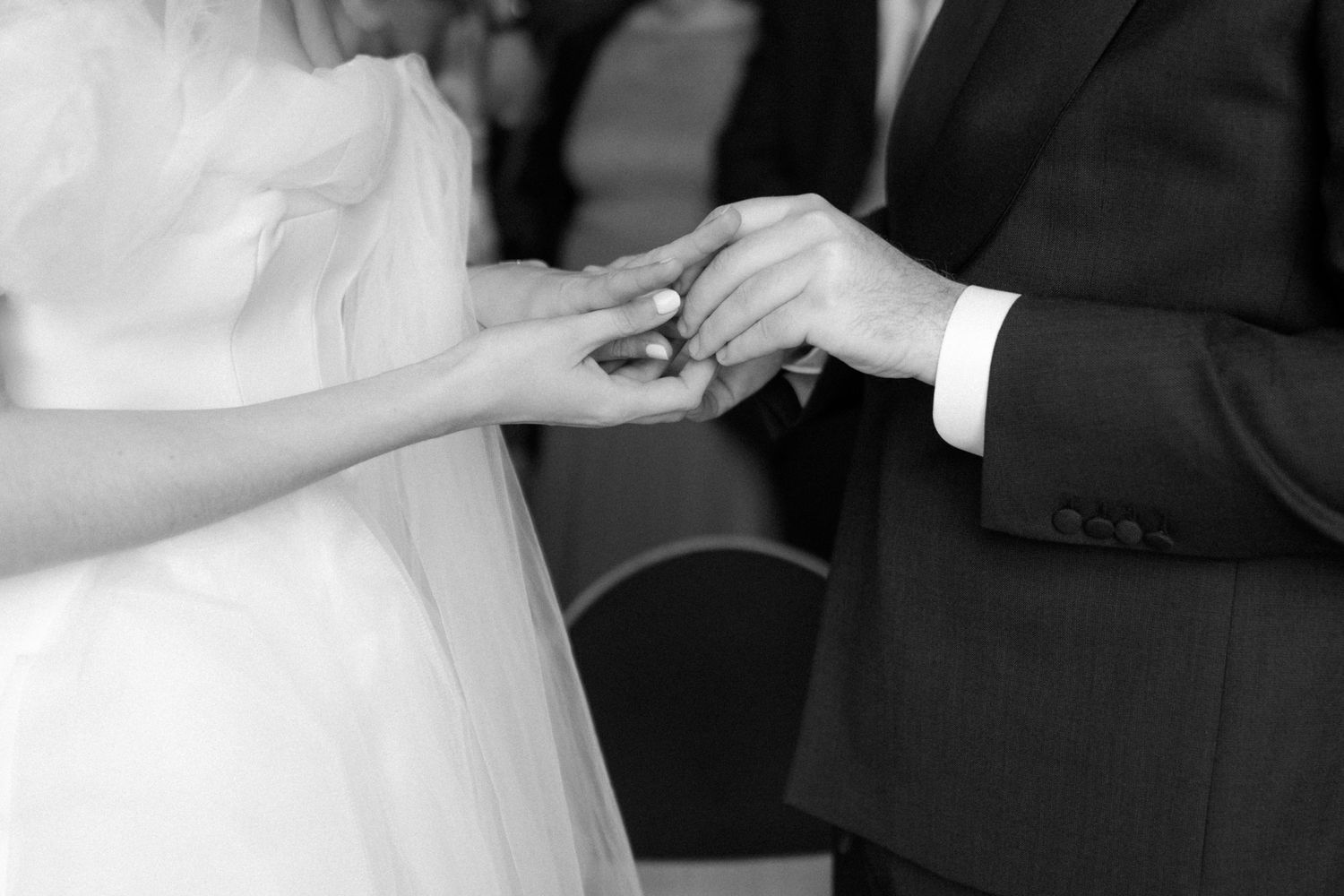 Close-up black and white image of a couple exchanging rings during a wedding ceremony.