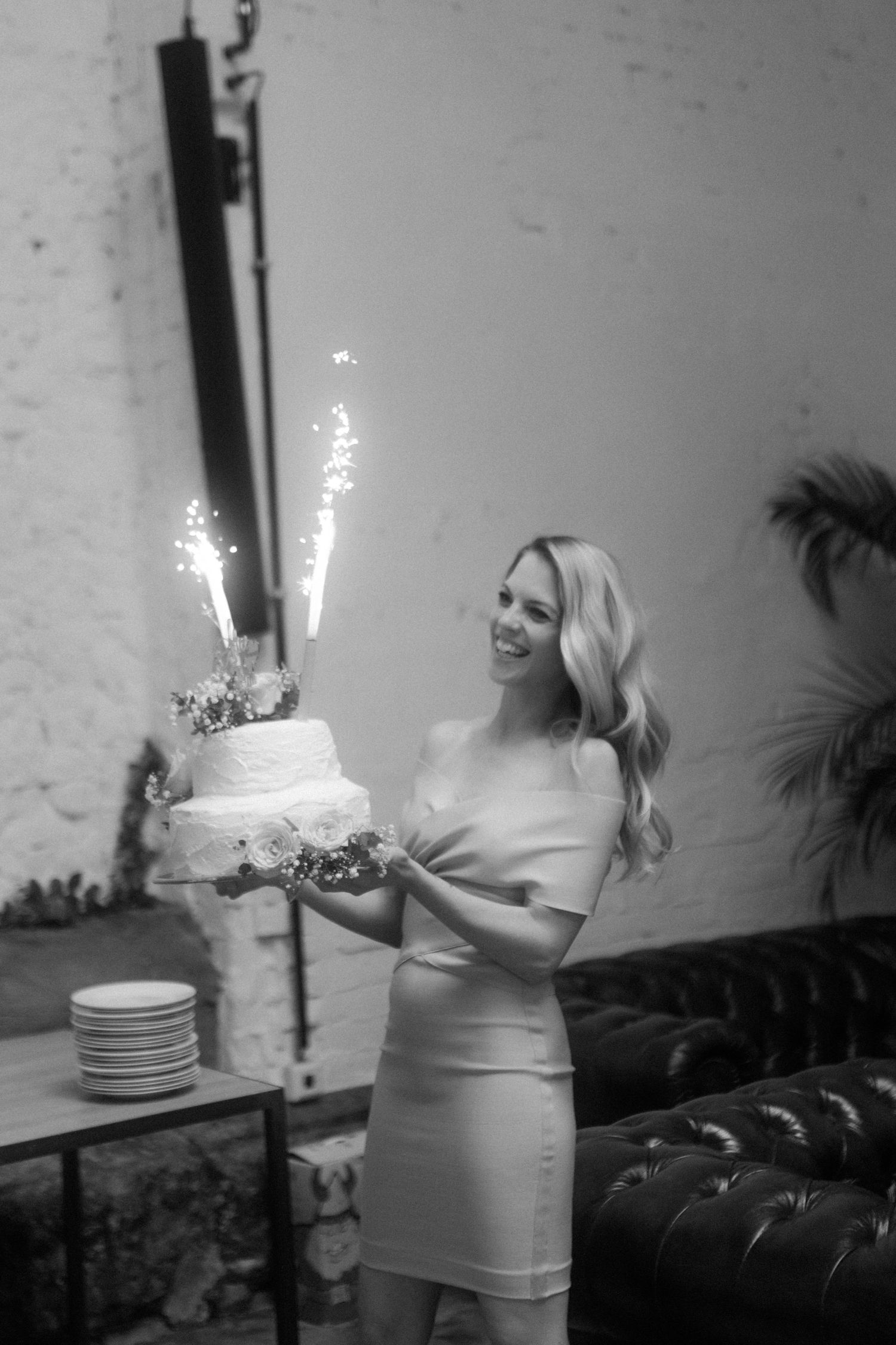 A black and white photo of someone holding a sparkling wedding cake at a reception.